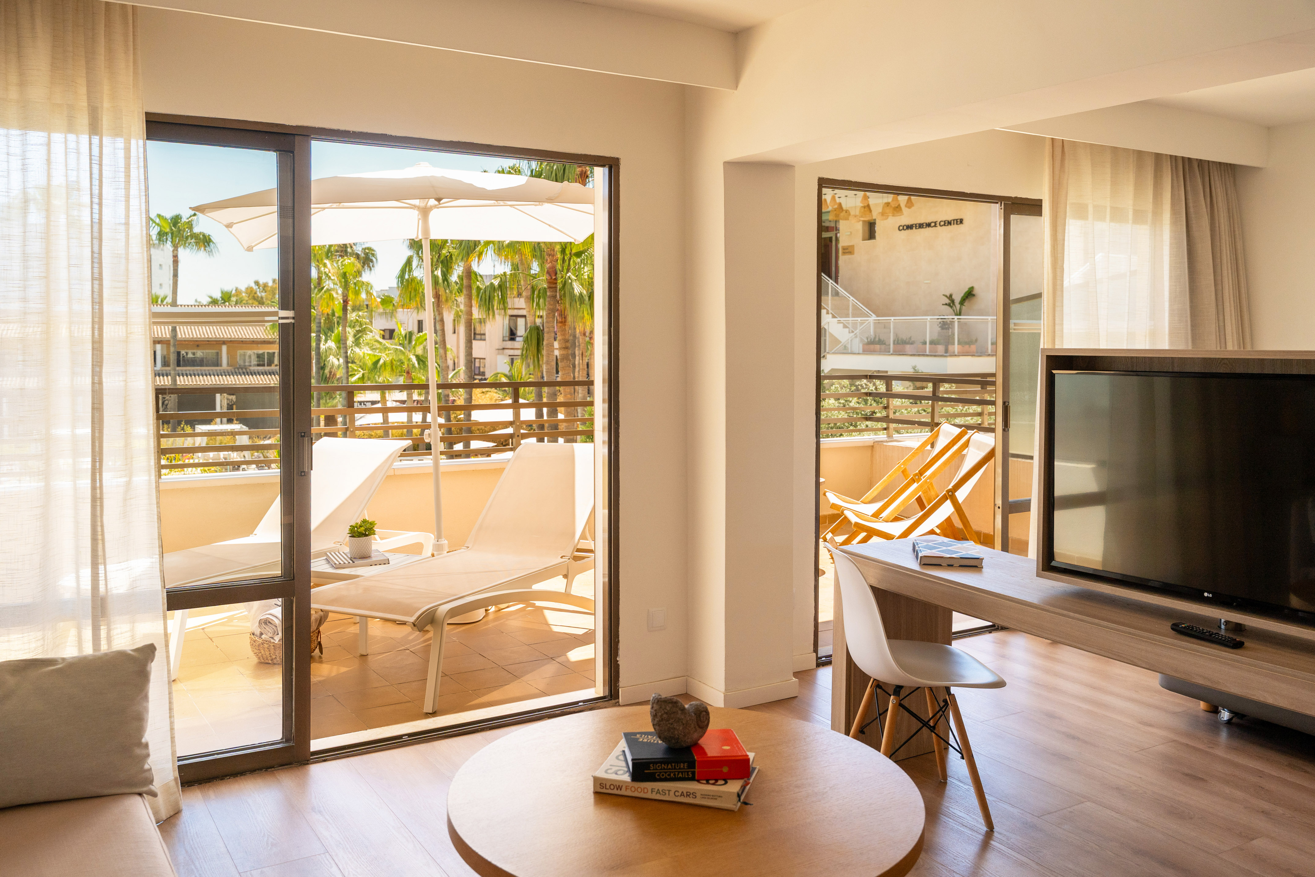 Sunny resort suite with balcony, lounge chairs, and tropical palm trees.