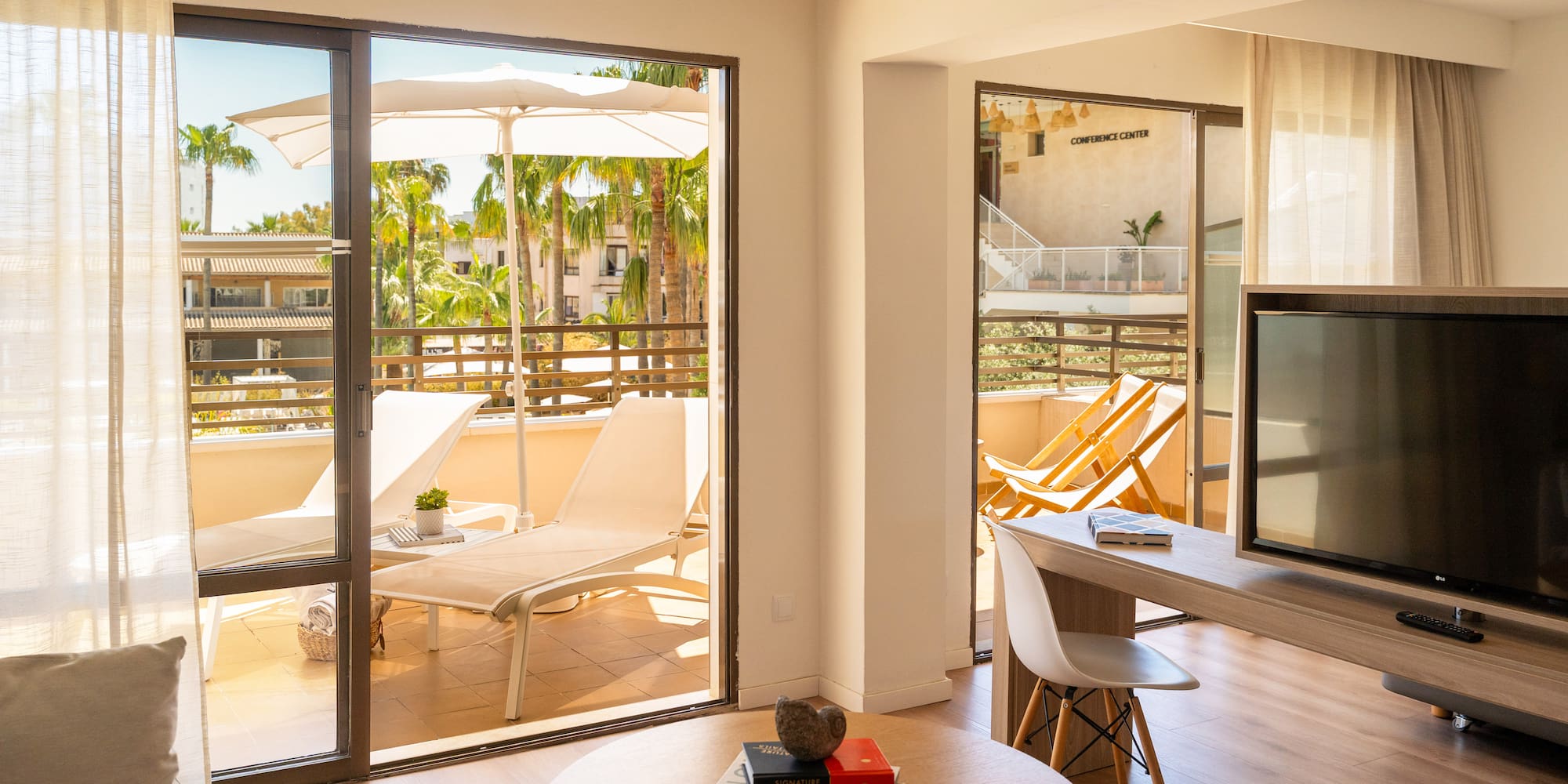Sunny resort suite with balcony, lounge chairs, and tropical palm trees.