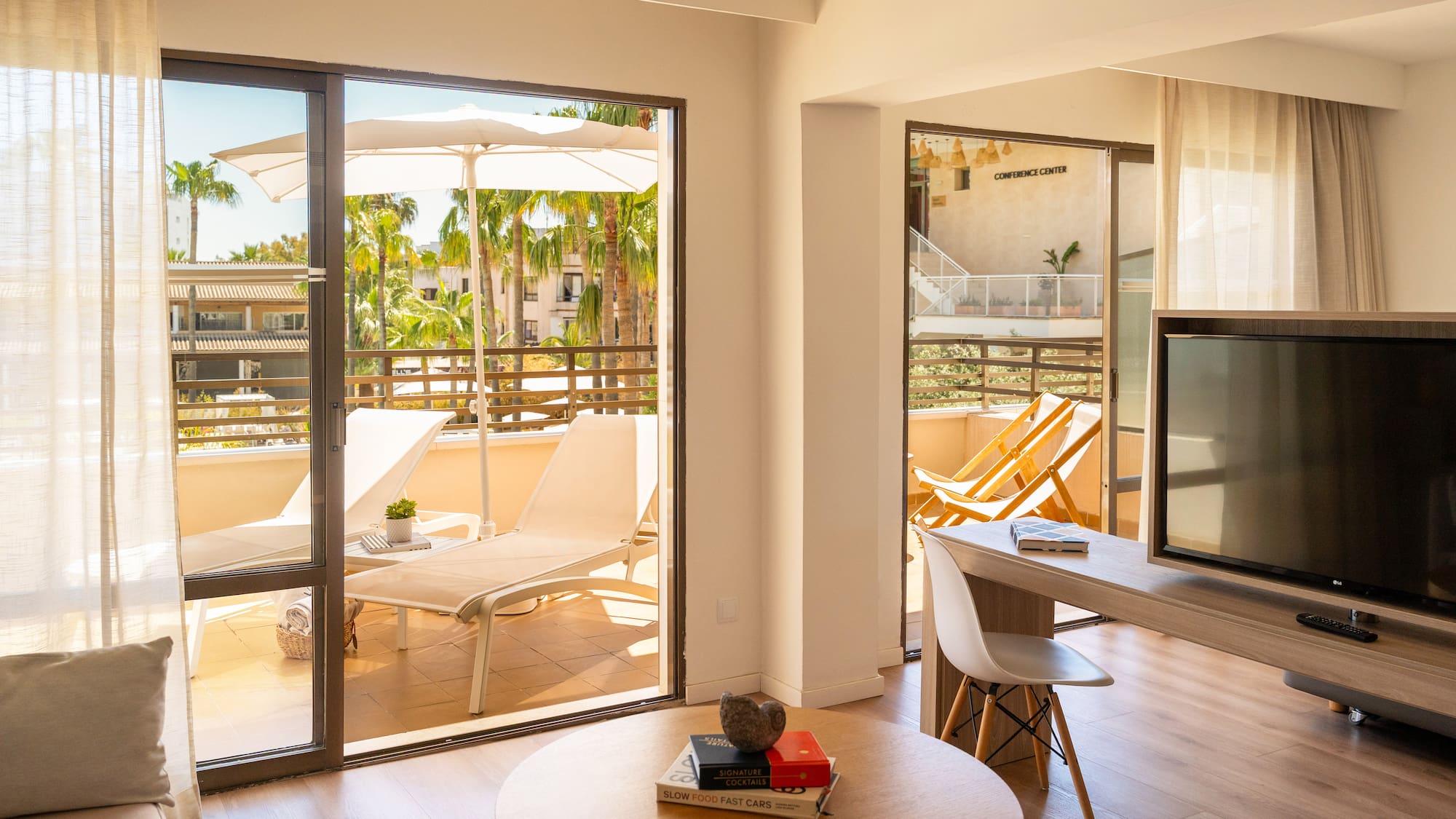 Sunny resort suite with balcony, lounge chairs, and tropical palm trees.