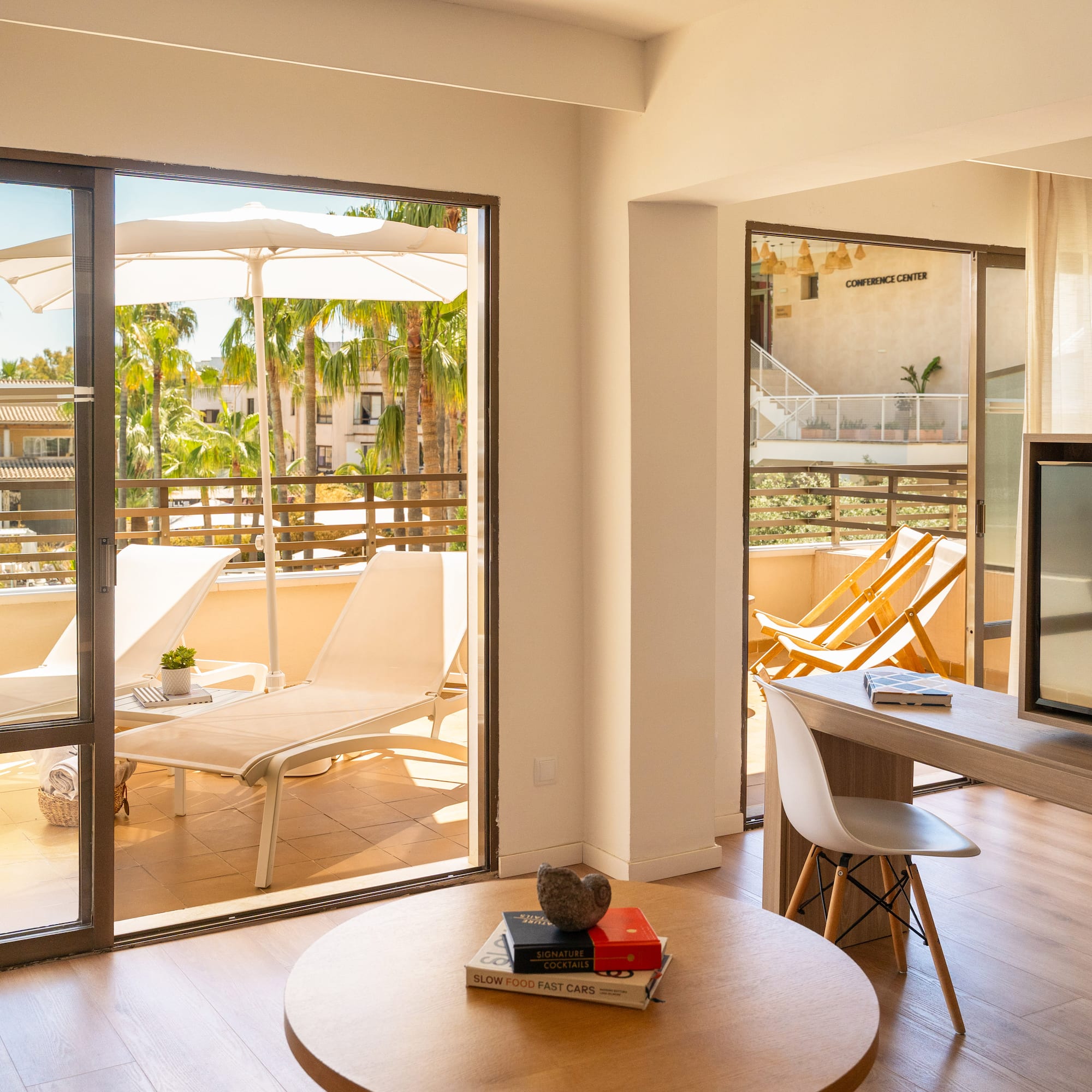 Sunny resort suite with balcony, lounge chairs, and tropical palm trees.