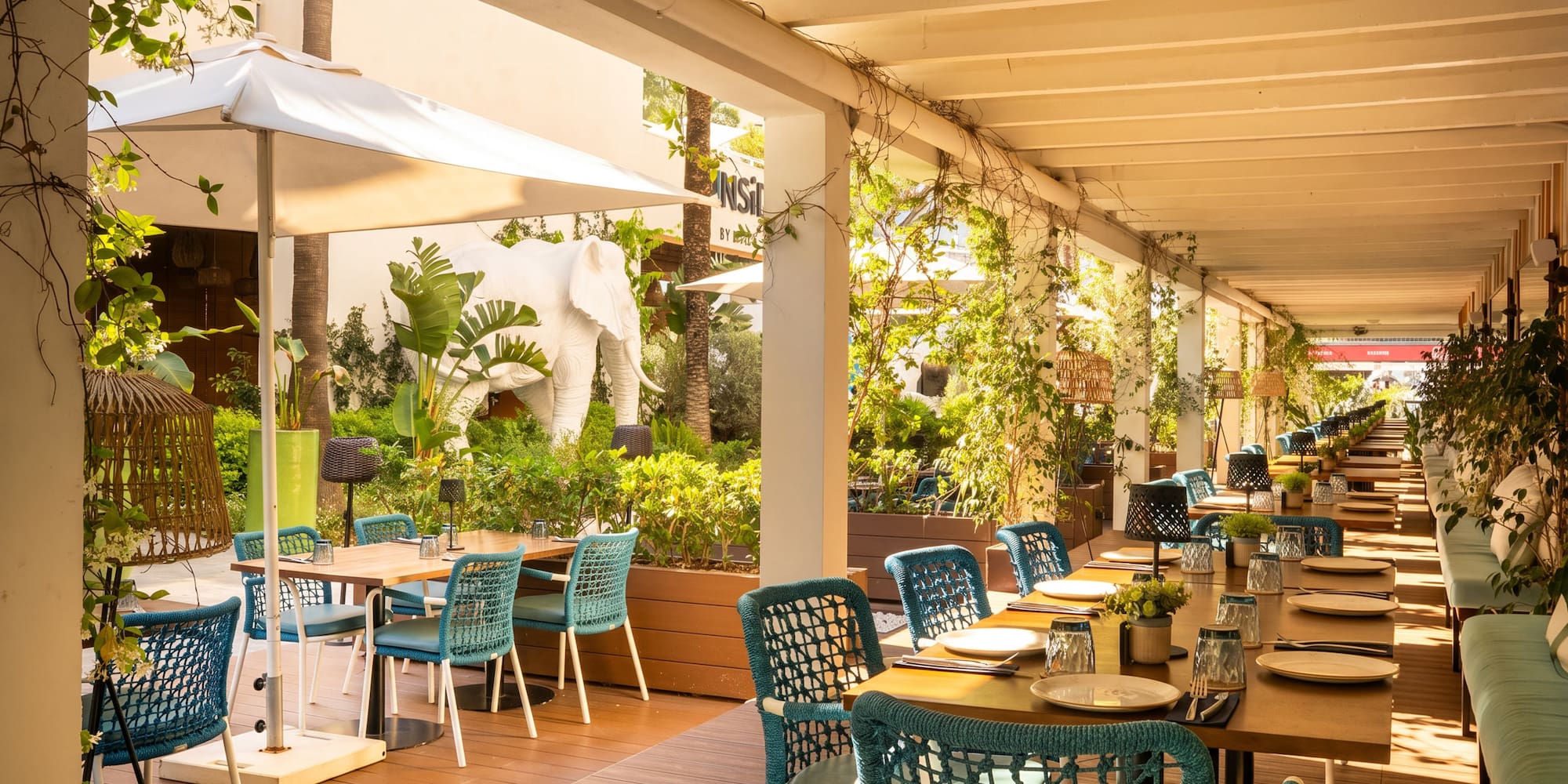 Tropical restaurant patio with teal chairs, set tables, and white elephant statue.