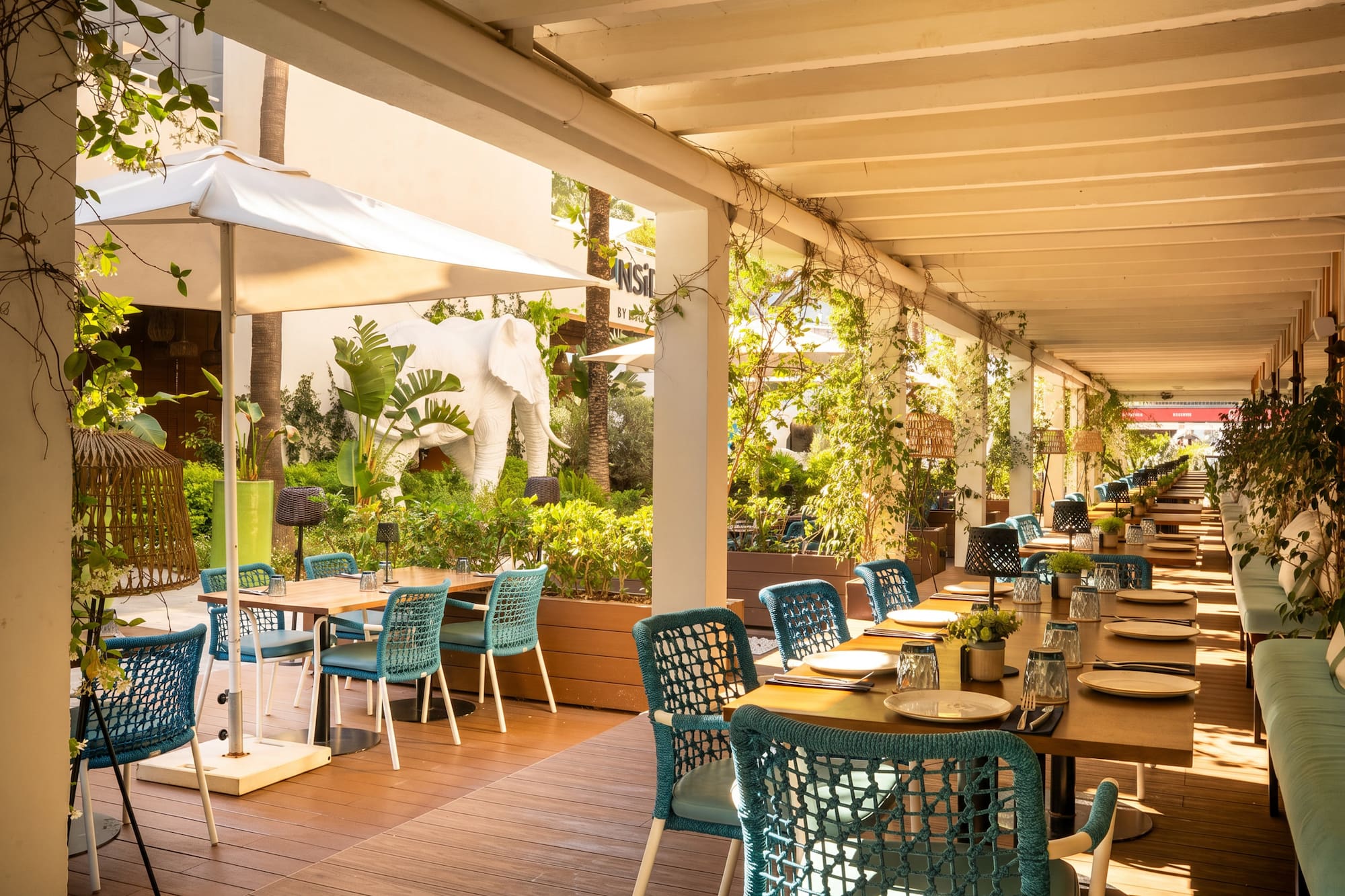 Tropical restaurant patio with teal chairs, set tables, and white elephant statue.
