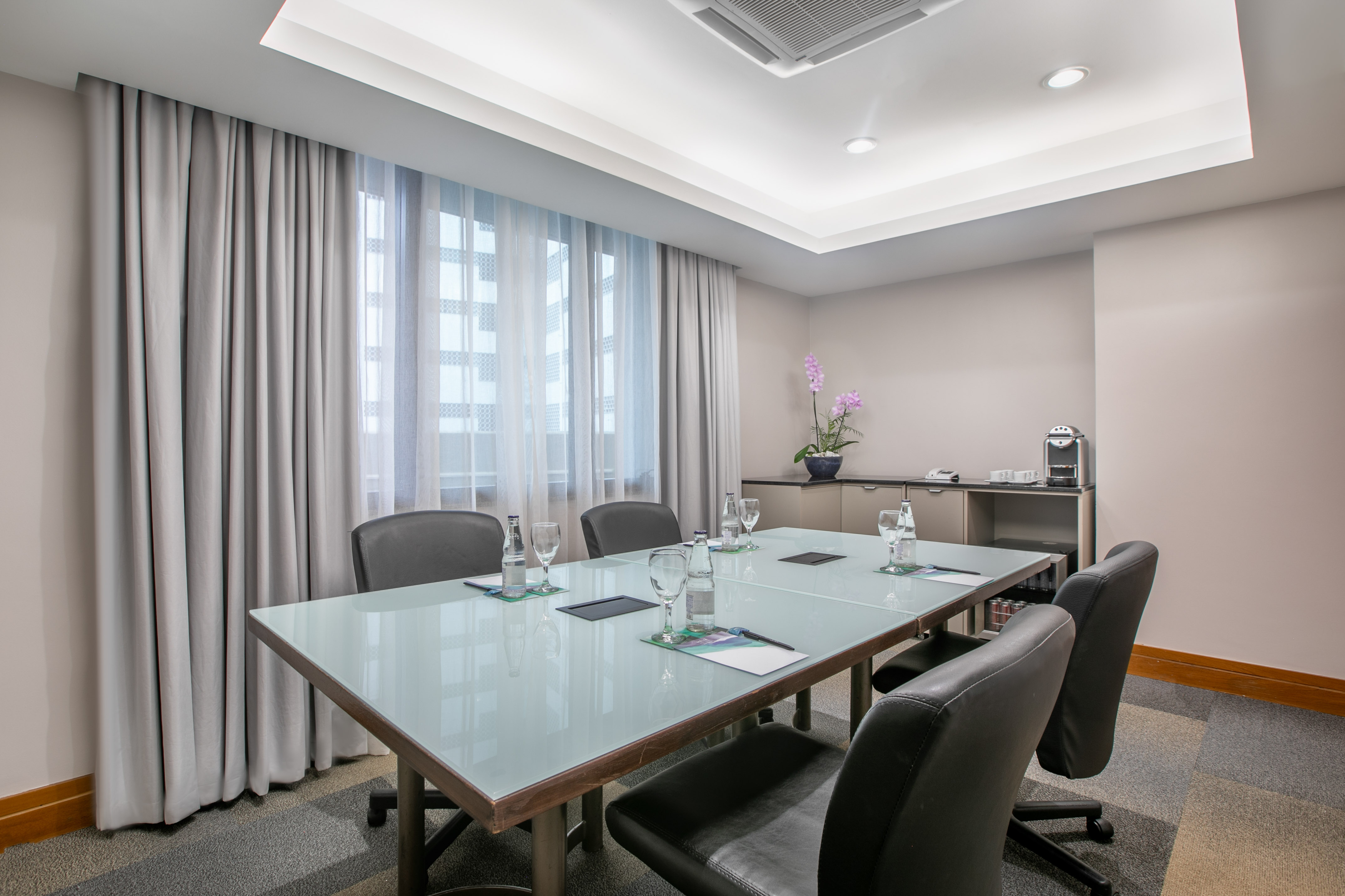 Professional conference room with glass table, chairs, window, and coffee station.