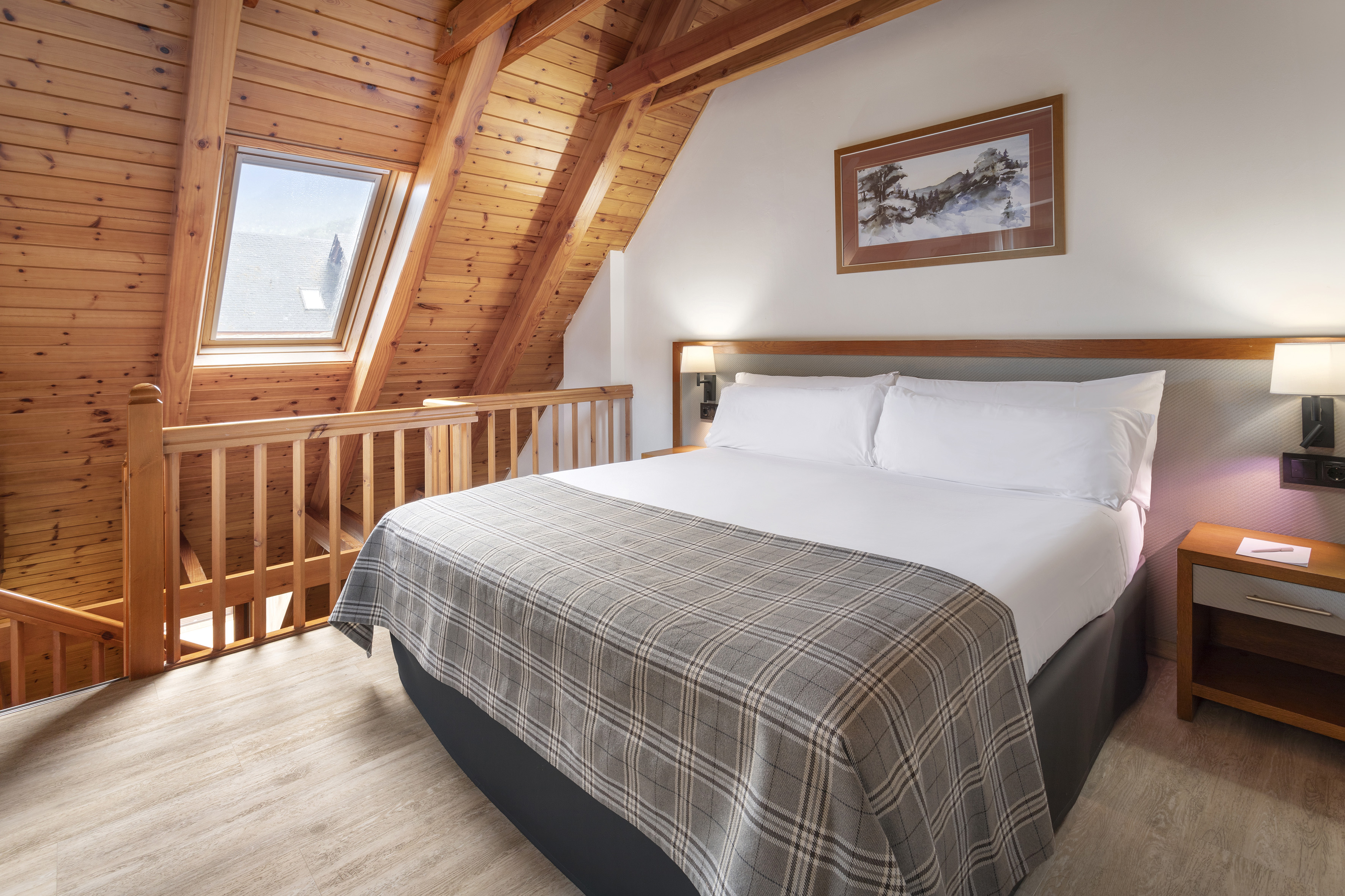 Loft bedroom with wooden ceiling, skylight, large bed, and cozy plaid throw.