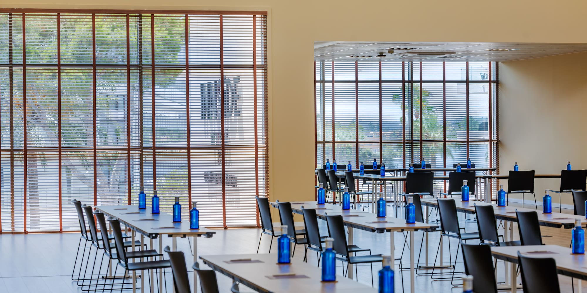 Modern meeting room setup: tables, chairs, blue bottles, large windows.