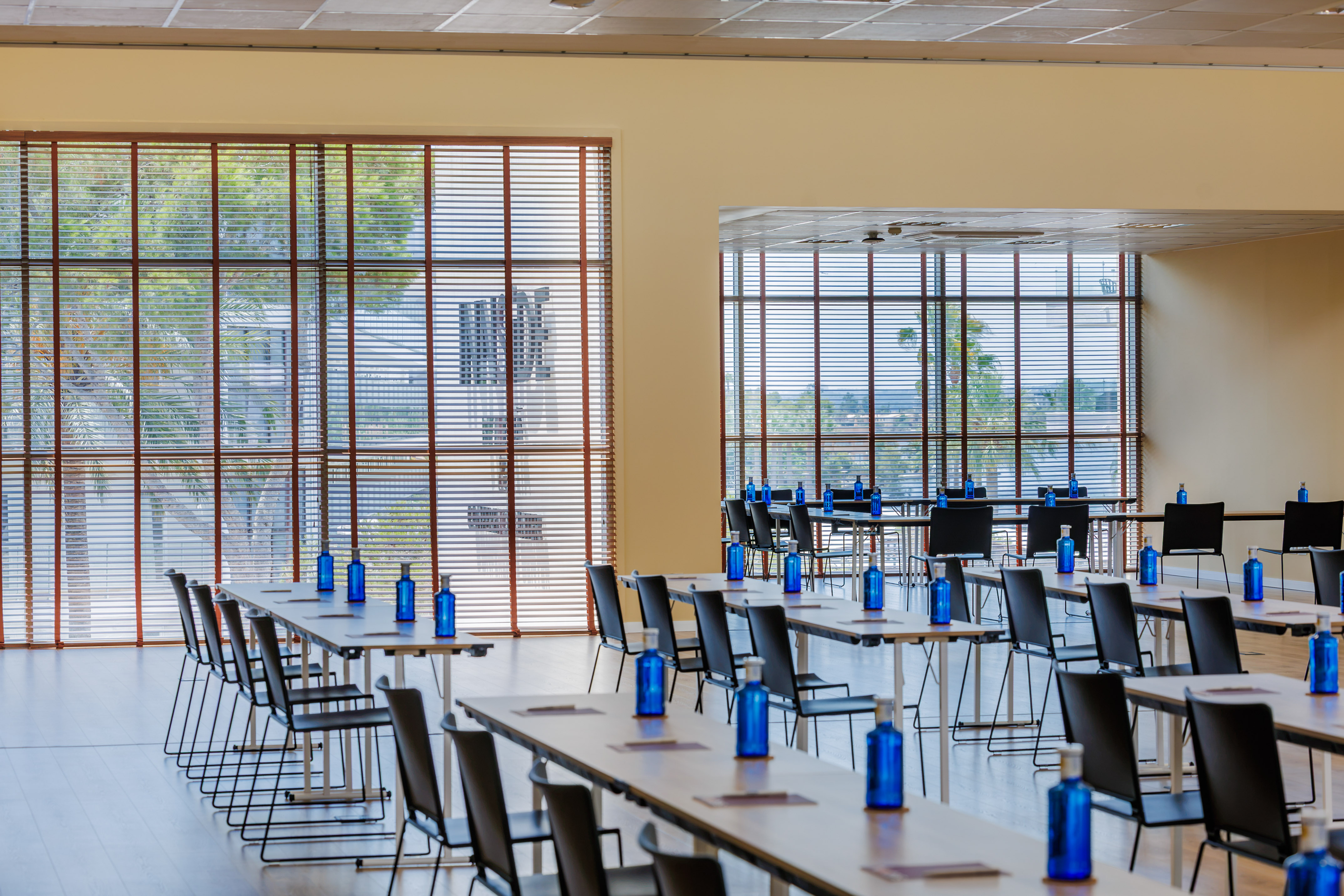 Modern meeting room setup: tables, chairs, blue bottles, large windows.