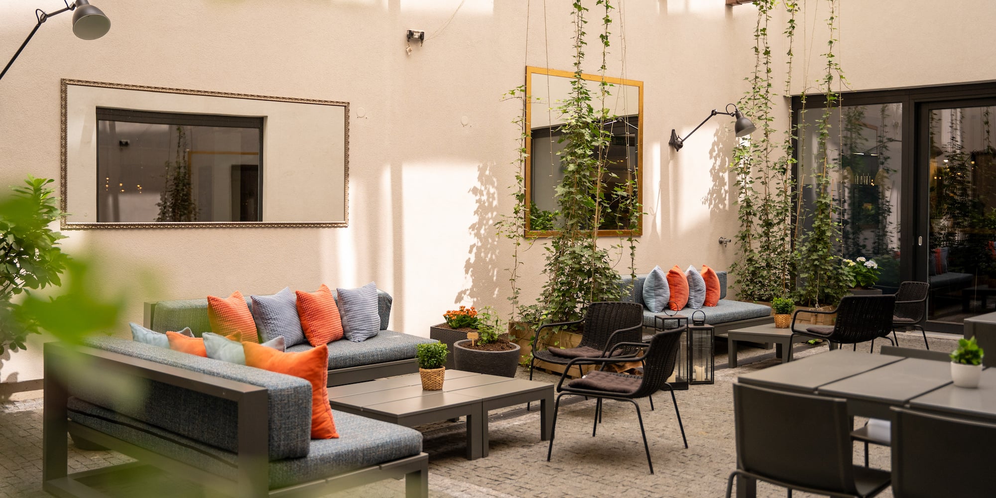 Modern outdoor patio lounge with sofas, tables, vibrant cushions, and climbing plants.