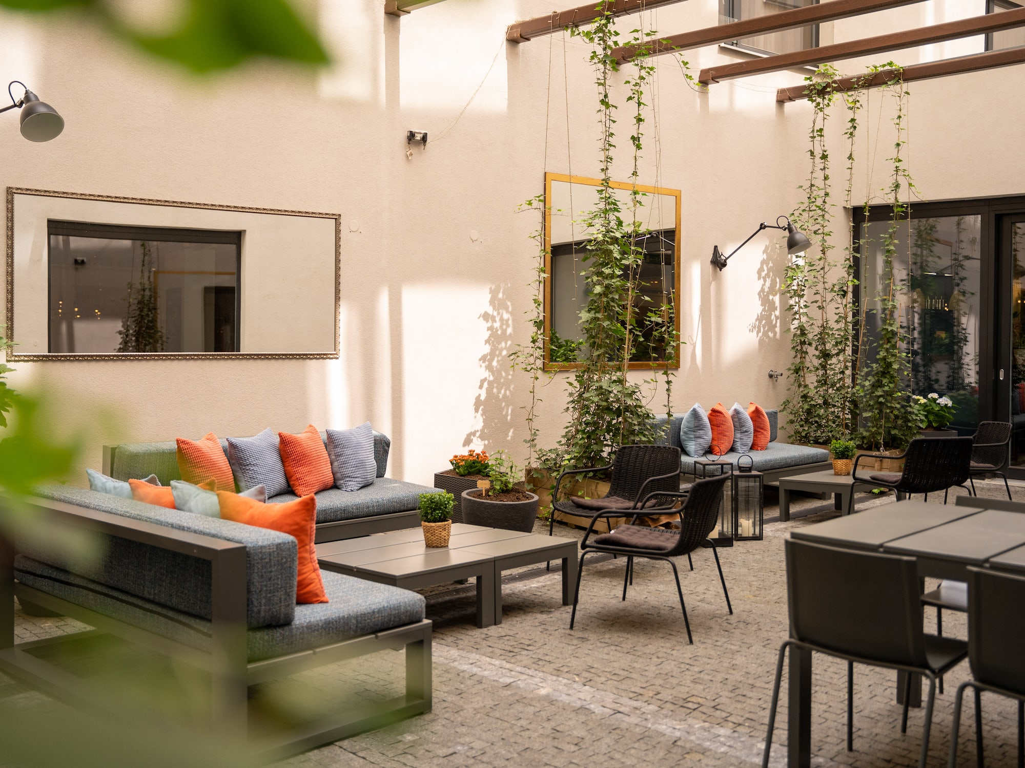 Modern outdoor patio lounge with sofas, tables, vibrant cushions, and climbing plants.