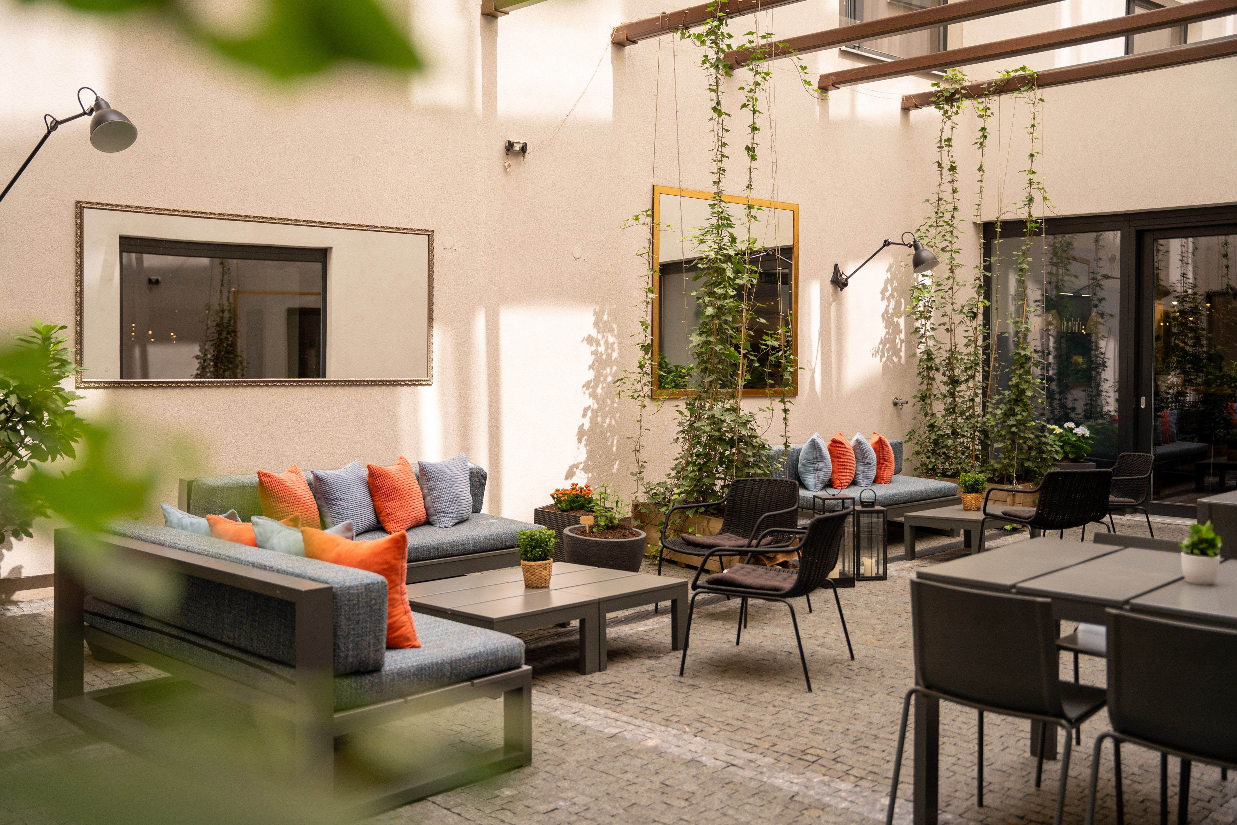 Modern outdoor patio lounge with sofas, tables, vibrant cushions, and climbing plants.