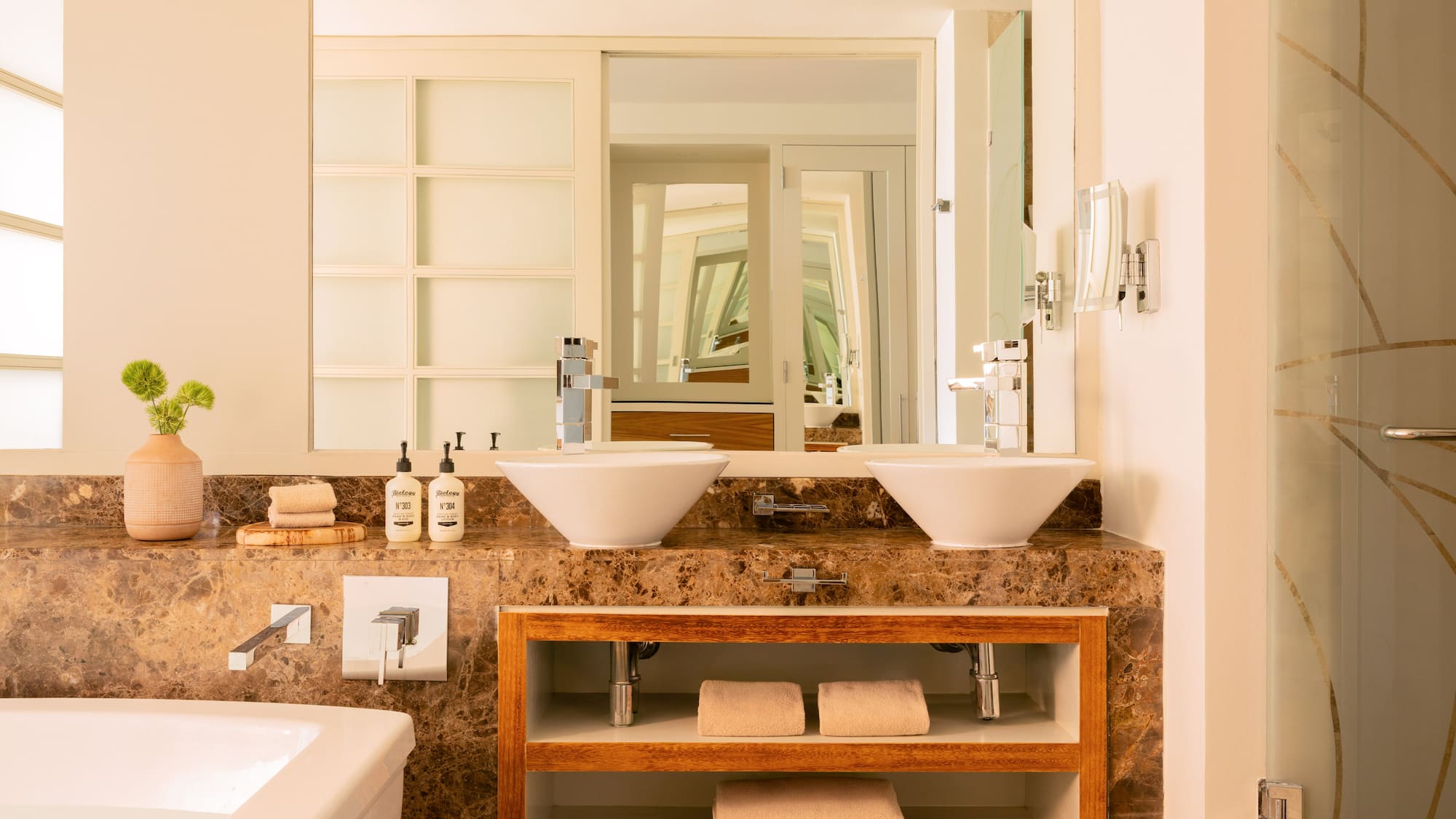 Luxury bathroom with double vessel sinks, marble counter, and wood shelves.