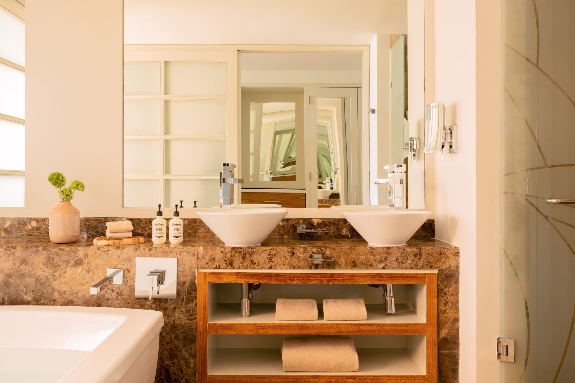Luxury bathroom with double vessel sinks, marble counter, and wood shelves.