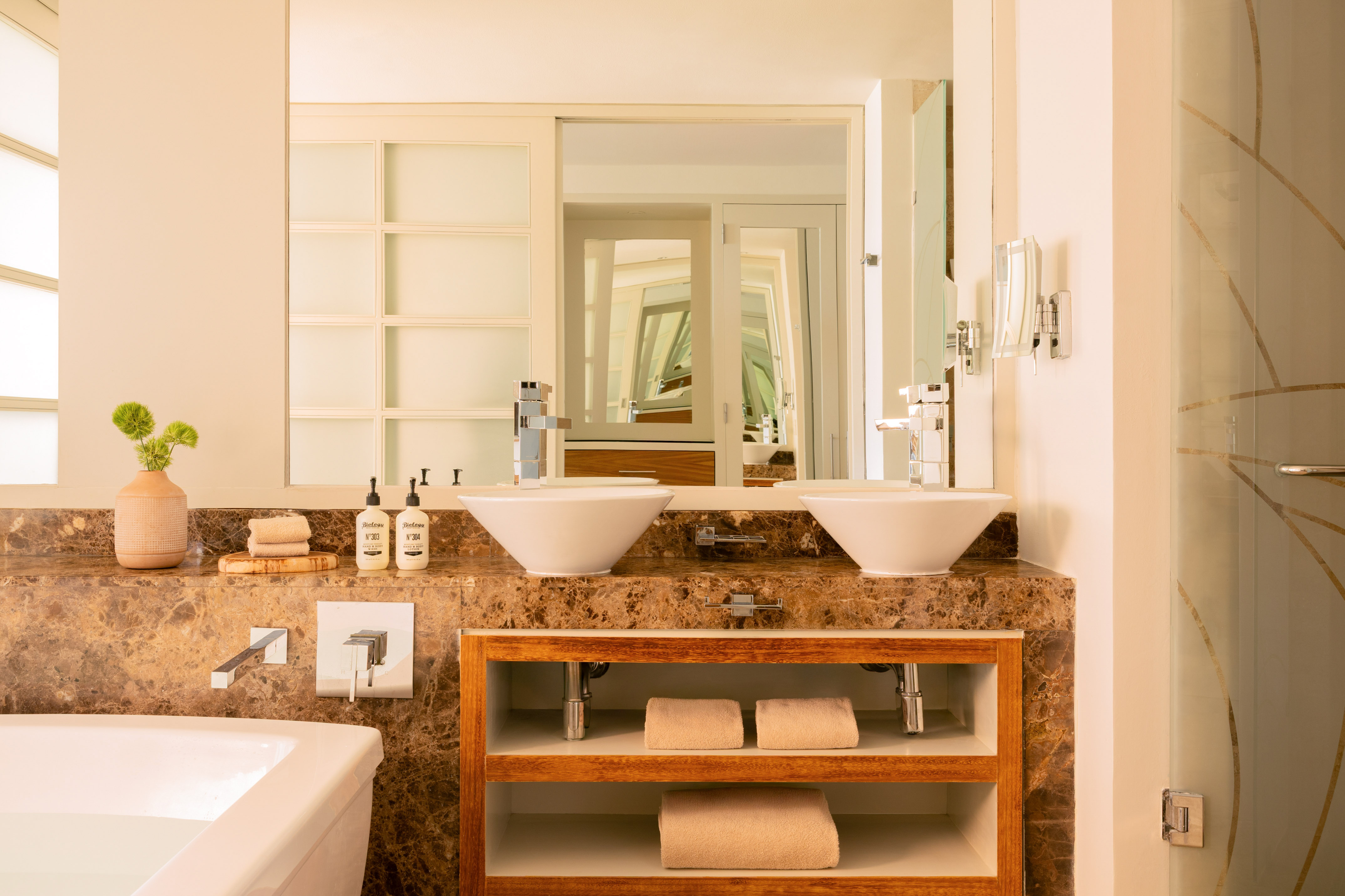 Luxury bathroom with double vessel sinks, marble counter, and wood shelves.