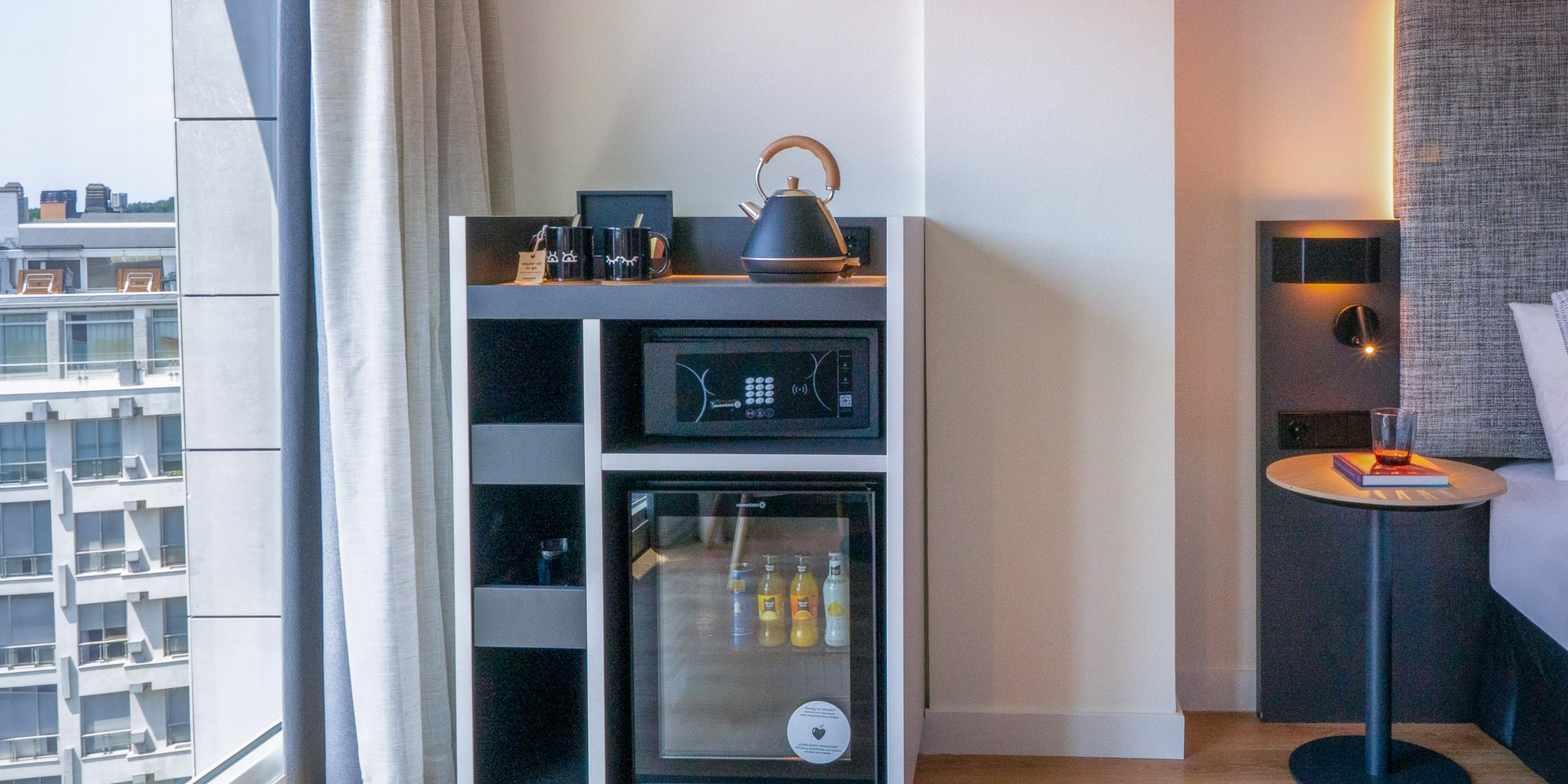 Mueble minibar moderno en habitación de hotel con hervidor, caja fuerte, vista ciudad.