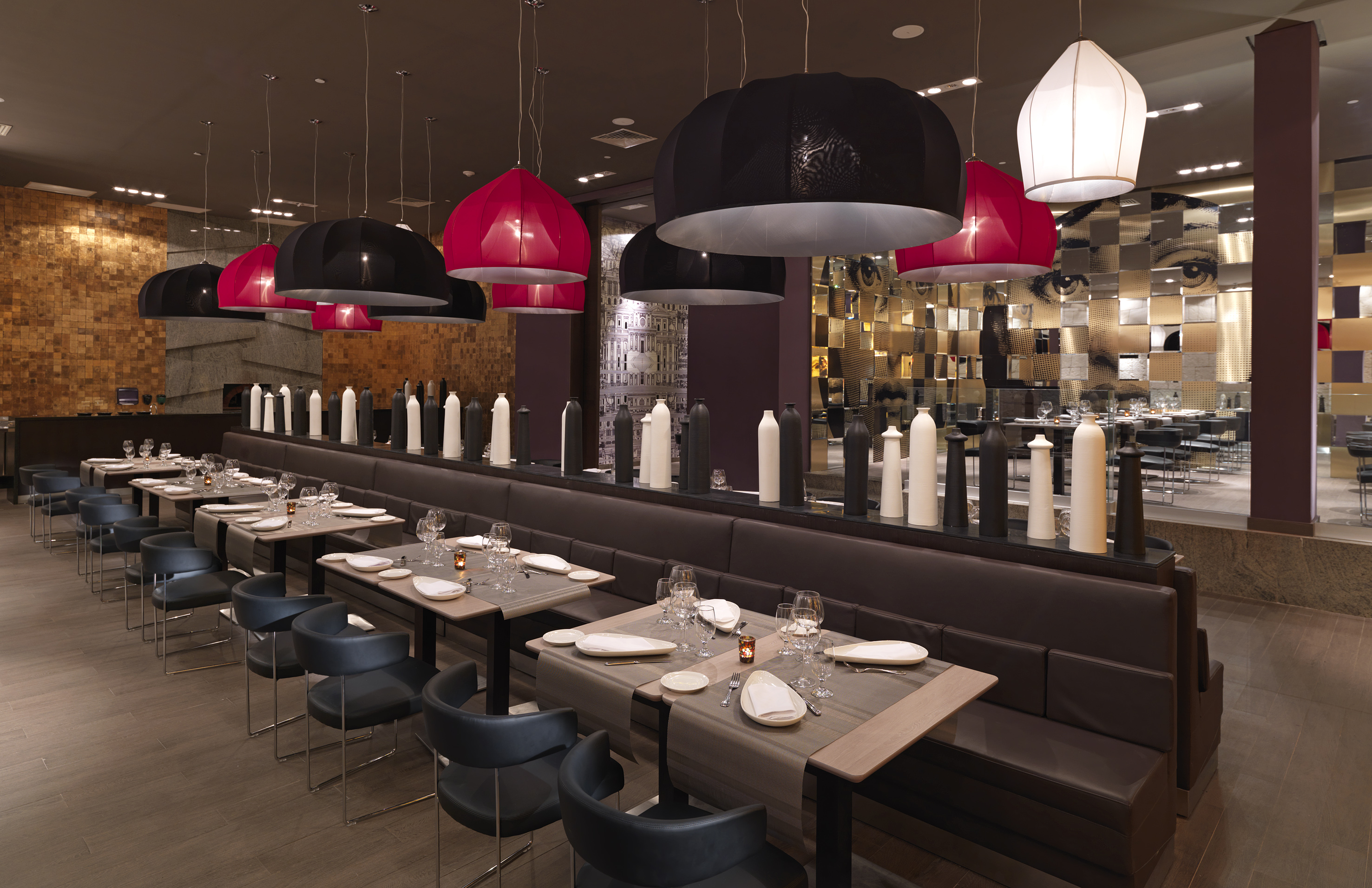 Modern restaurant with black and red pendant lights, set tables, booth seating.