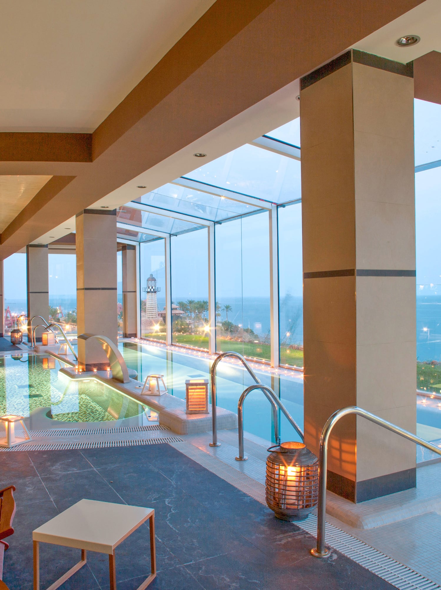 Spa lujoso con piscina interior, vista al mar, palmeras y faro.