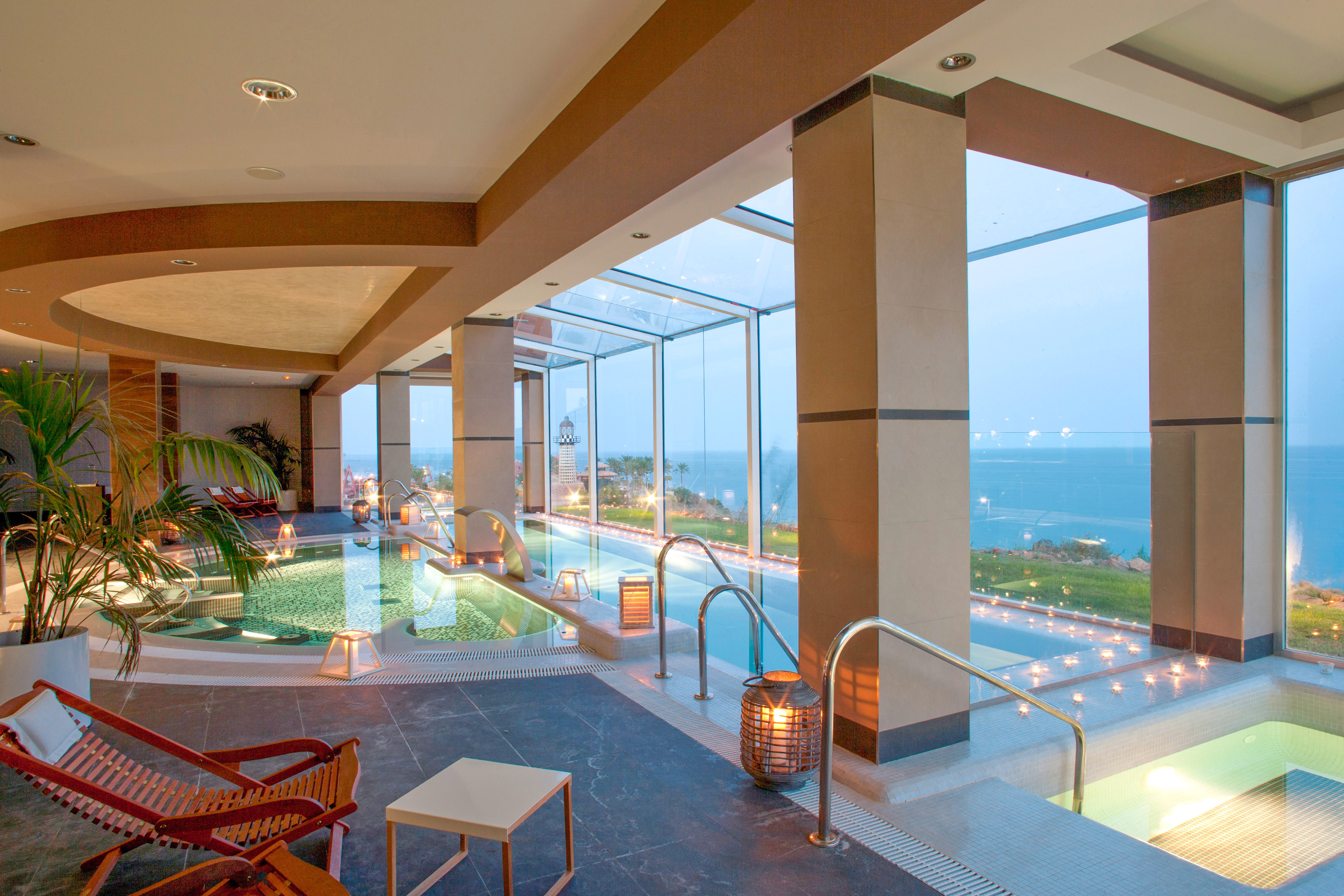 Spa lujoso con piscina interior, vista al mar, palmeras y faro.