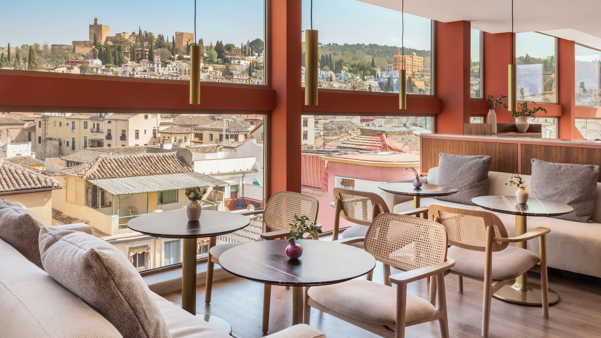 Modern cafe interior with panoramic Granada city view, Alhambra fortress in distance.