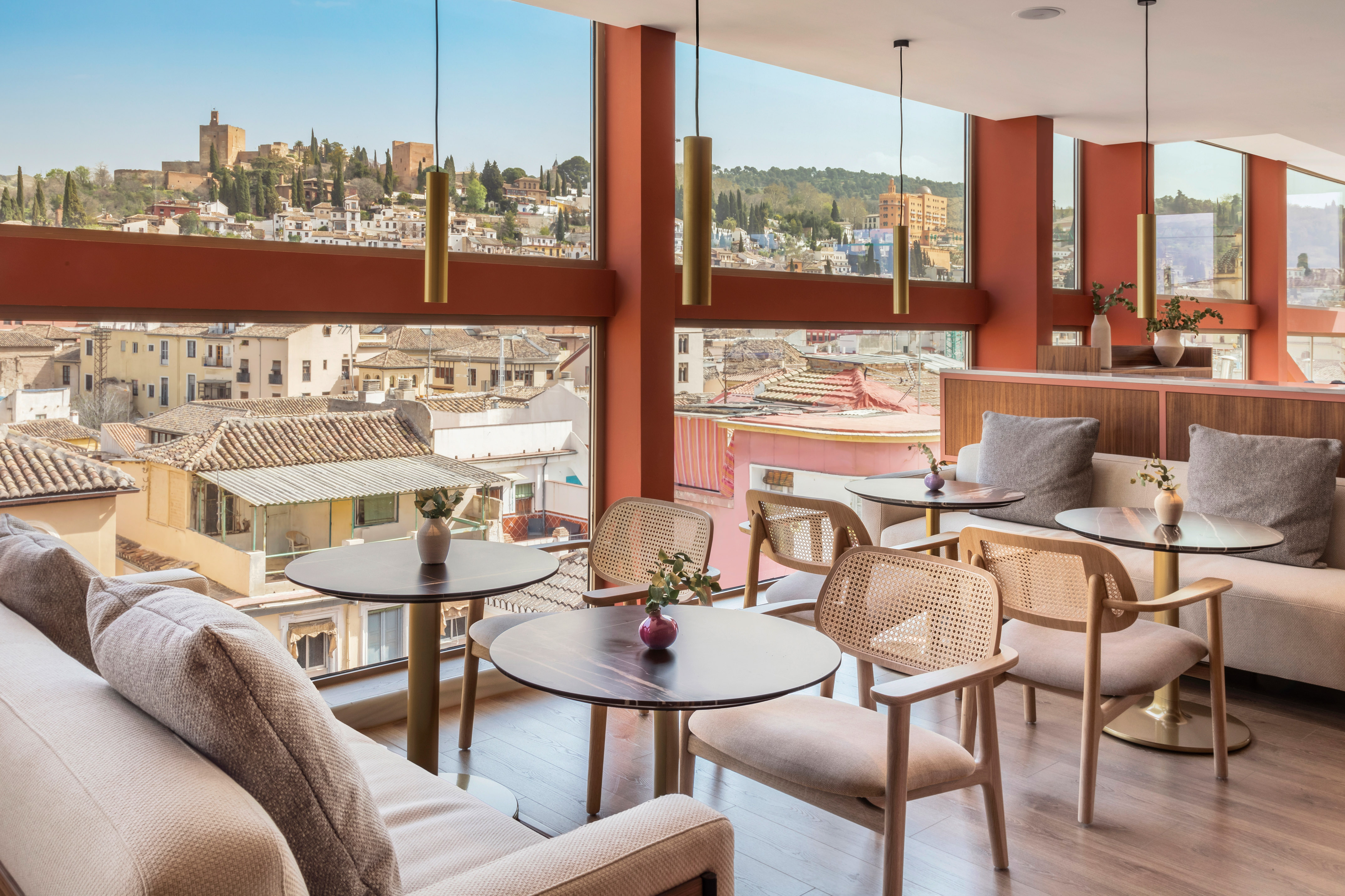 Modern cafe interior with panoramic Granada city view, Alhambra fortress in distance.