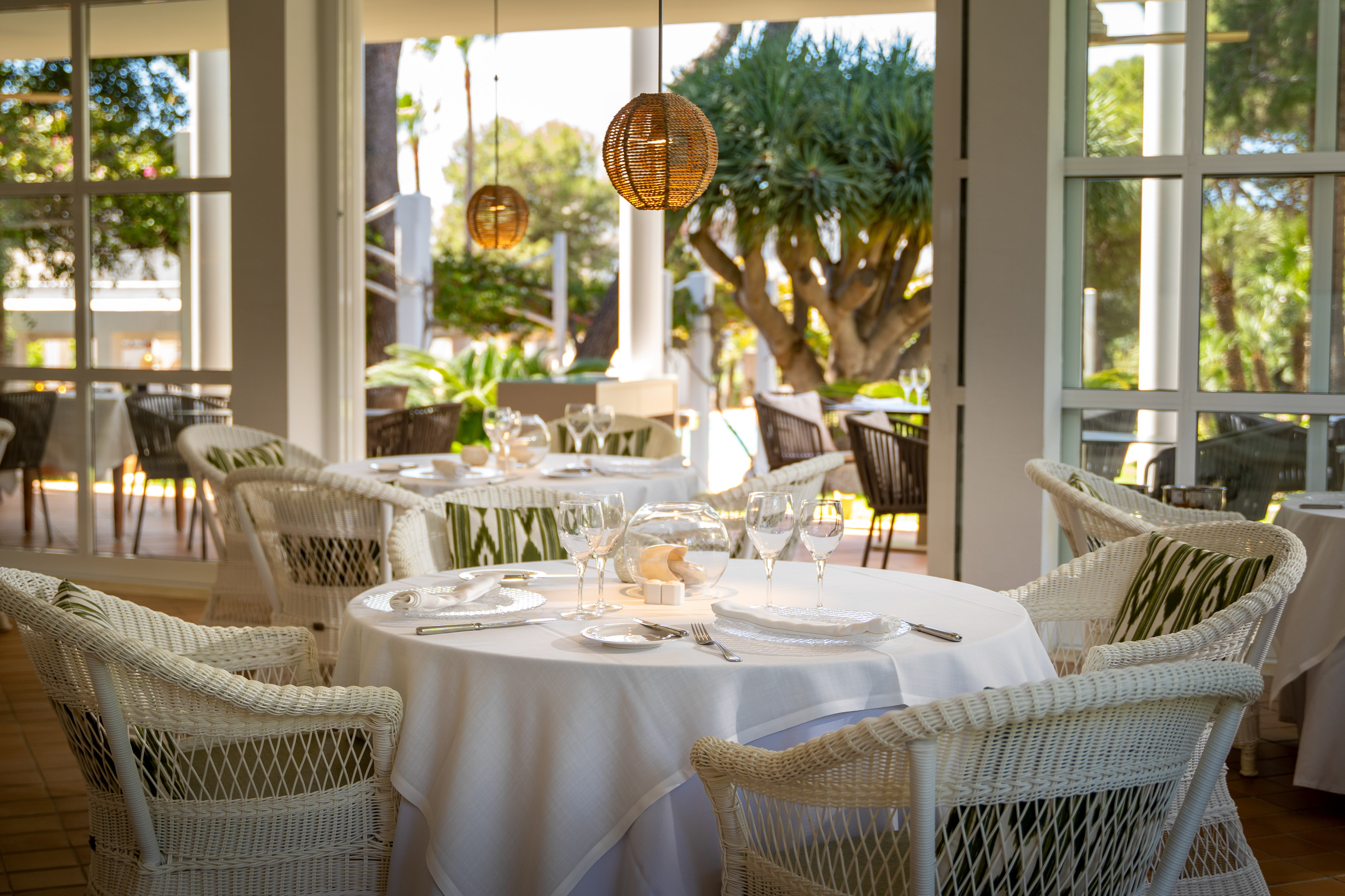 Elegant restaurant dining with white wicker chairs and scenic garden view.