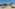 Mediterranean resort deck with ocean view, stylish daybeds, and olive trees.