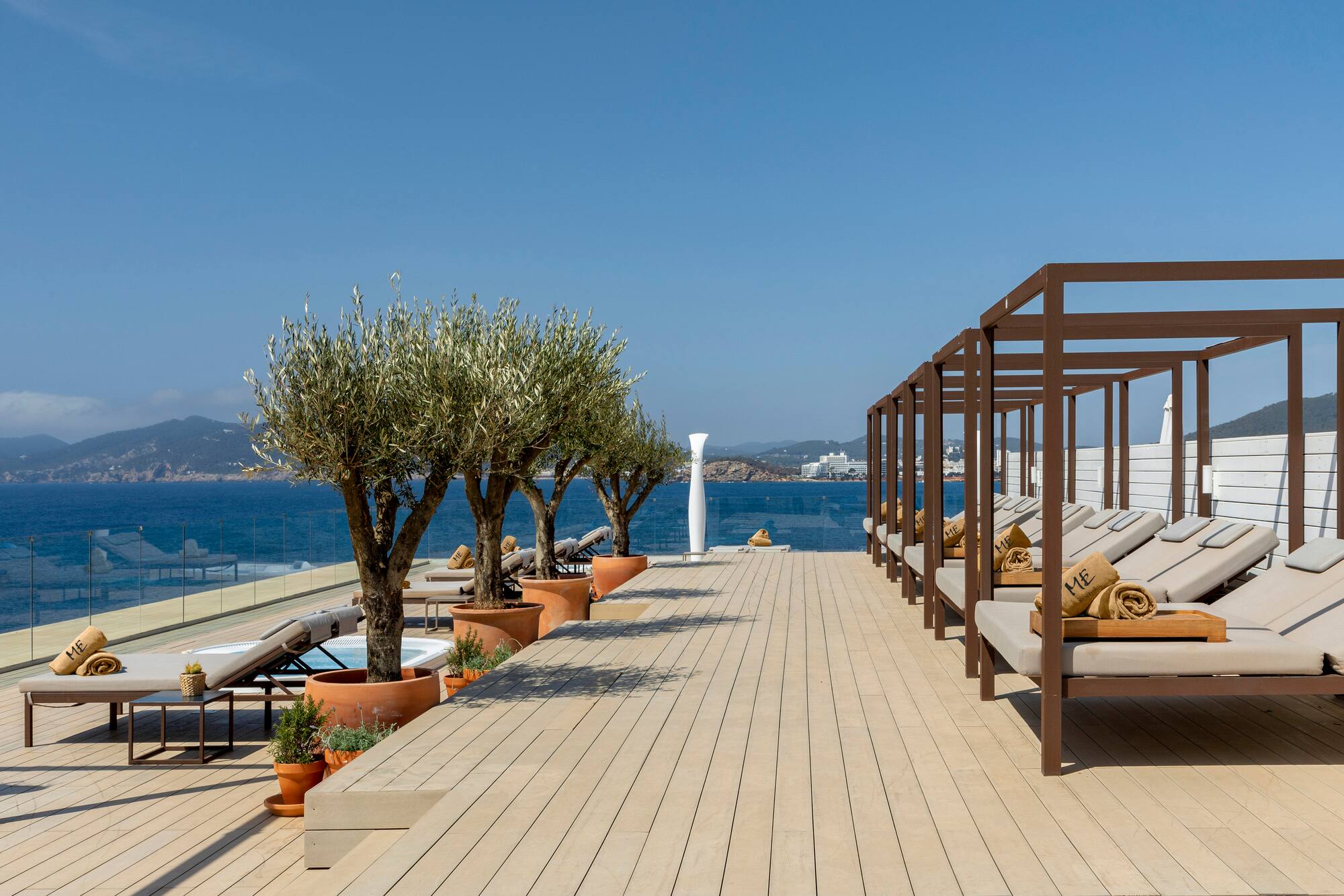 Mediterranean resort deck with ocean view, stylish daybeds, and olive trees.