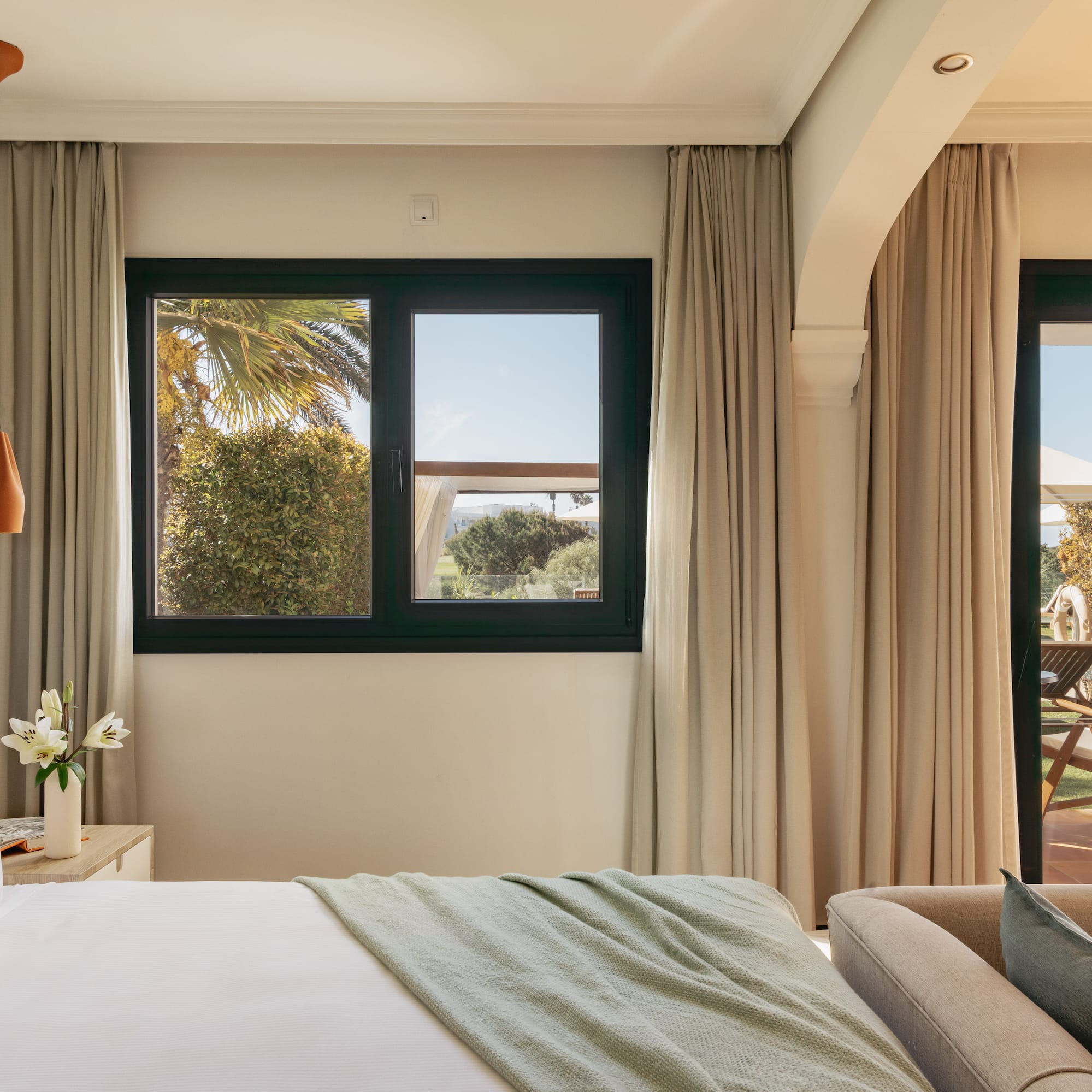 Bright hotel bedroom with bed, window overlooking garden, and private patio.
