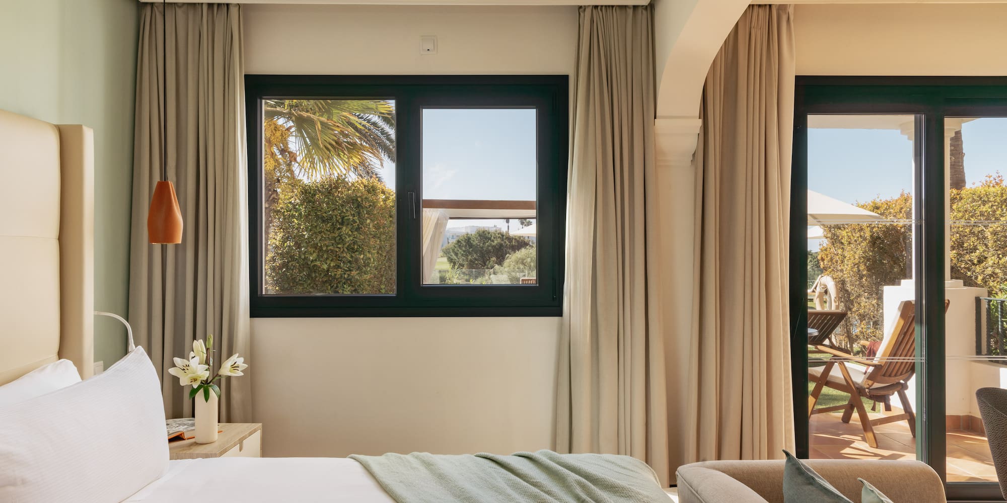 Bright hotel bedroom with bed, window overlooking garden, and private patio.