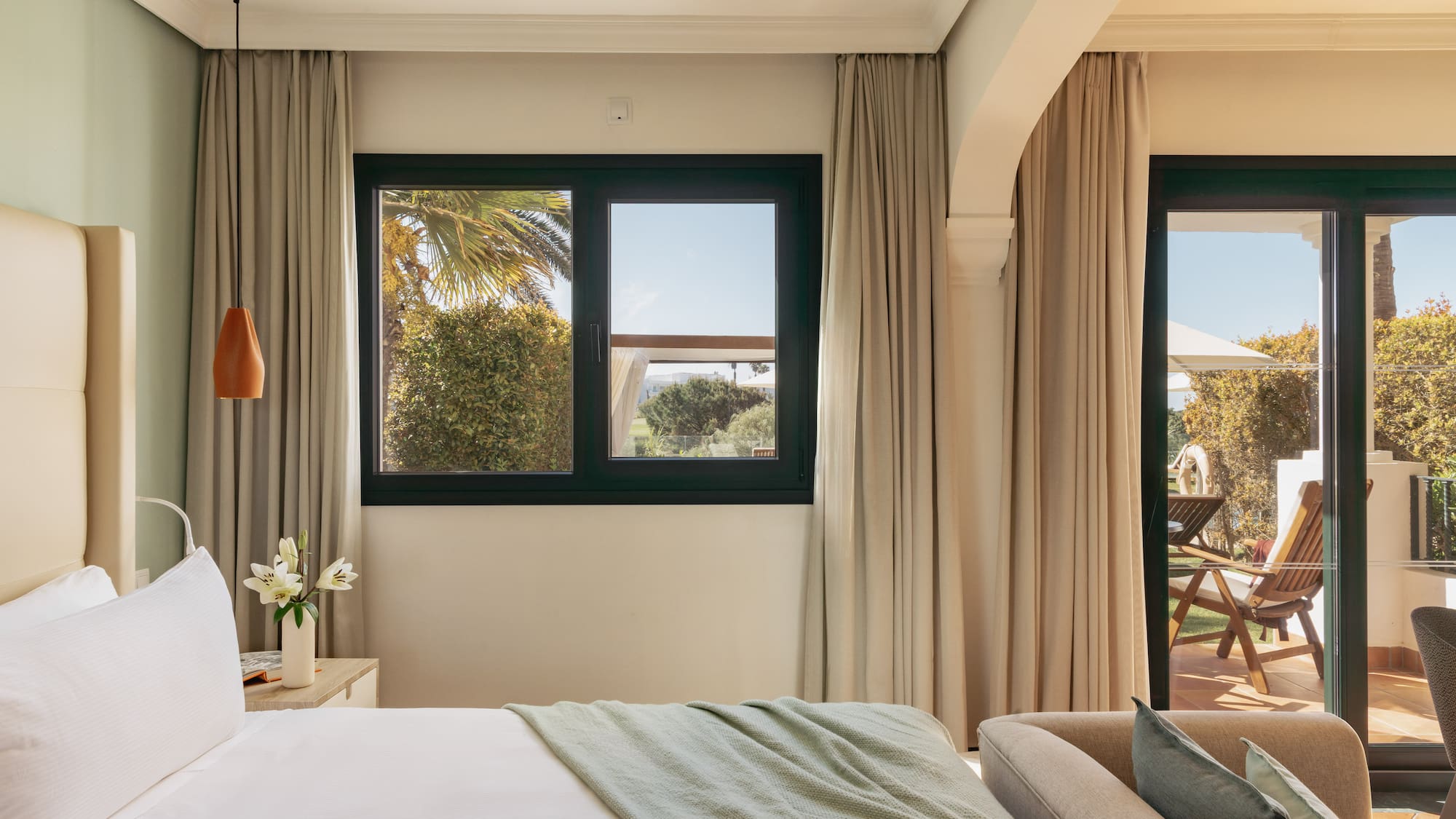 Bright hotel bedroom with bed, window overlooking garden, and private patio.