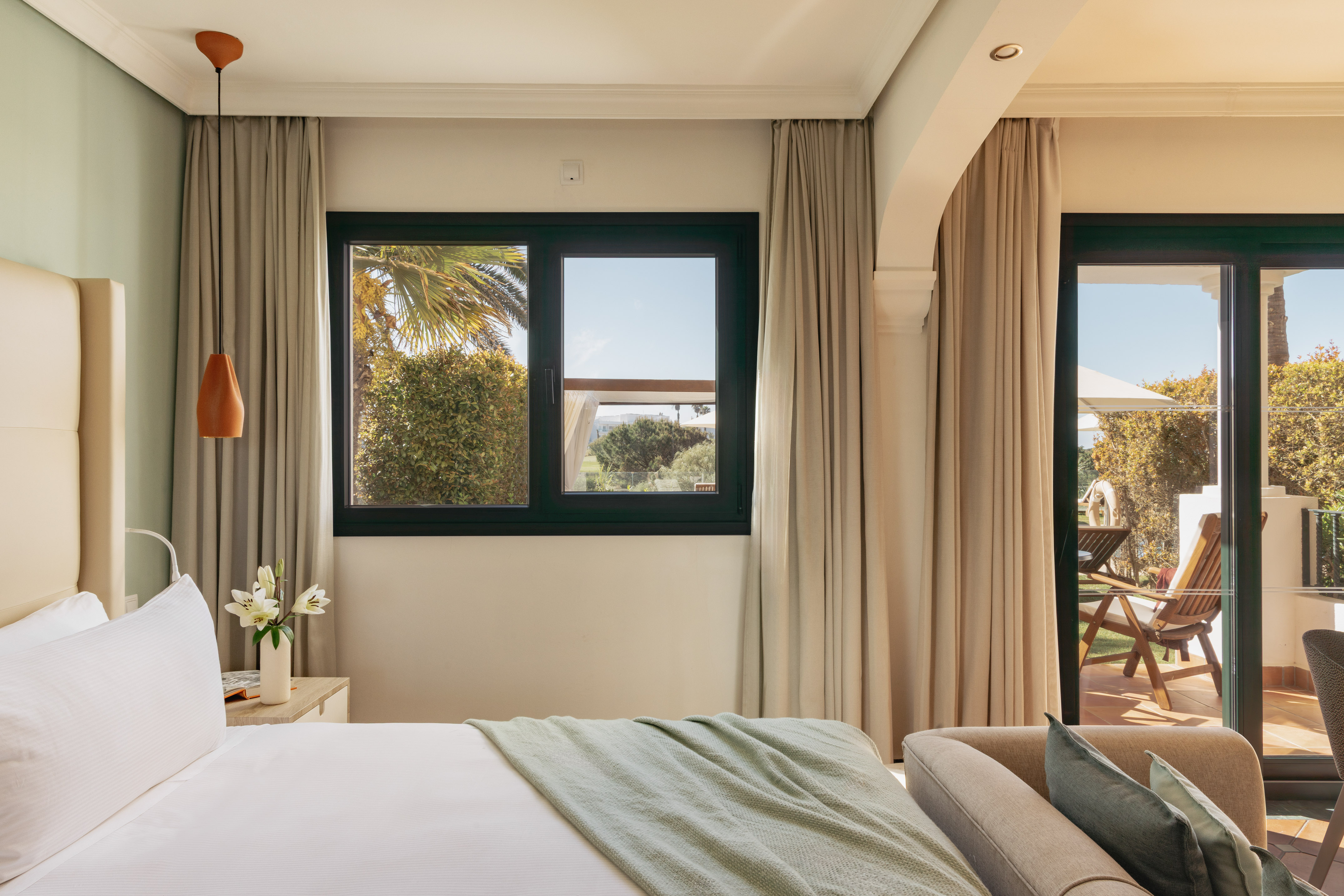 Bright hotel bedroom with bed, window overlooking garden, and private patio.