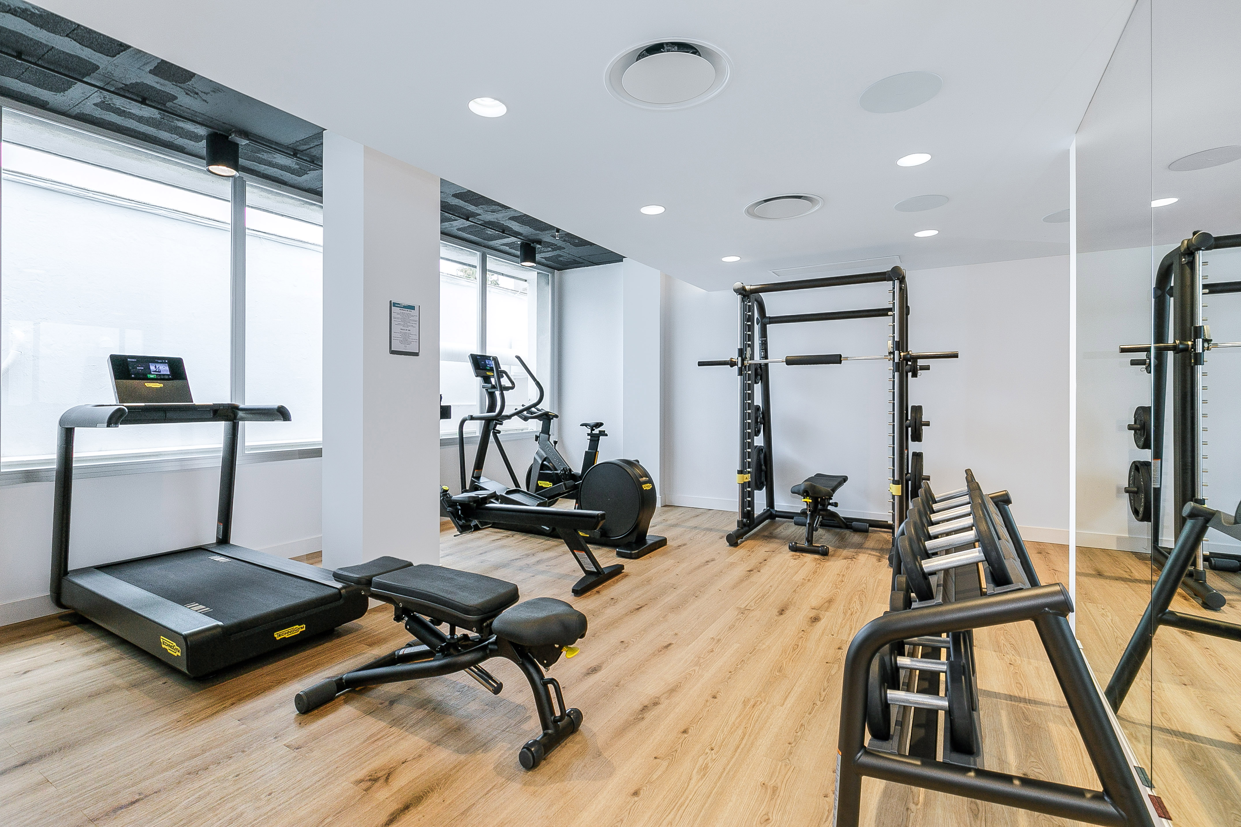 Modern gym with treadmill, cardio machines, dumbbells, and weight rack on wood floor.