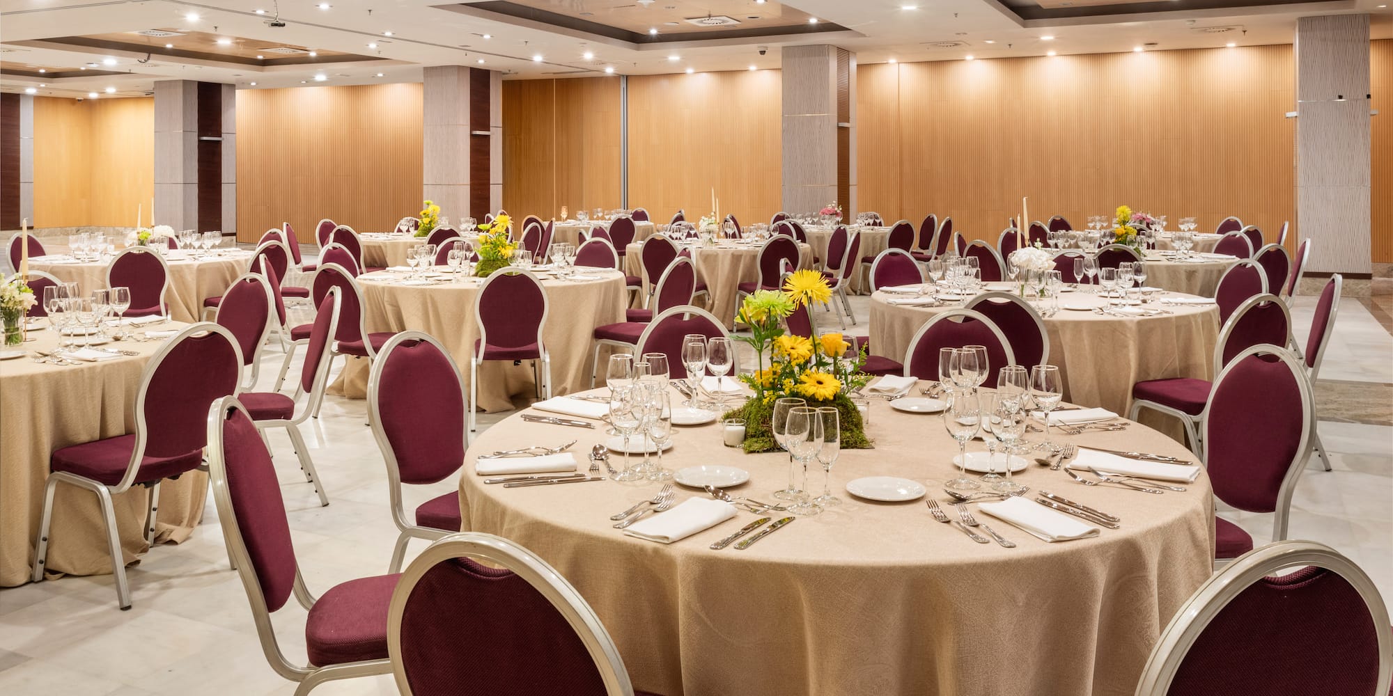 Banquet hall with round tables, maroon chairs, and yellow floral centerpieces.