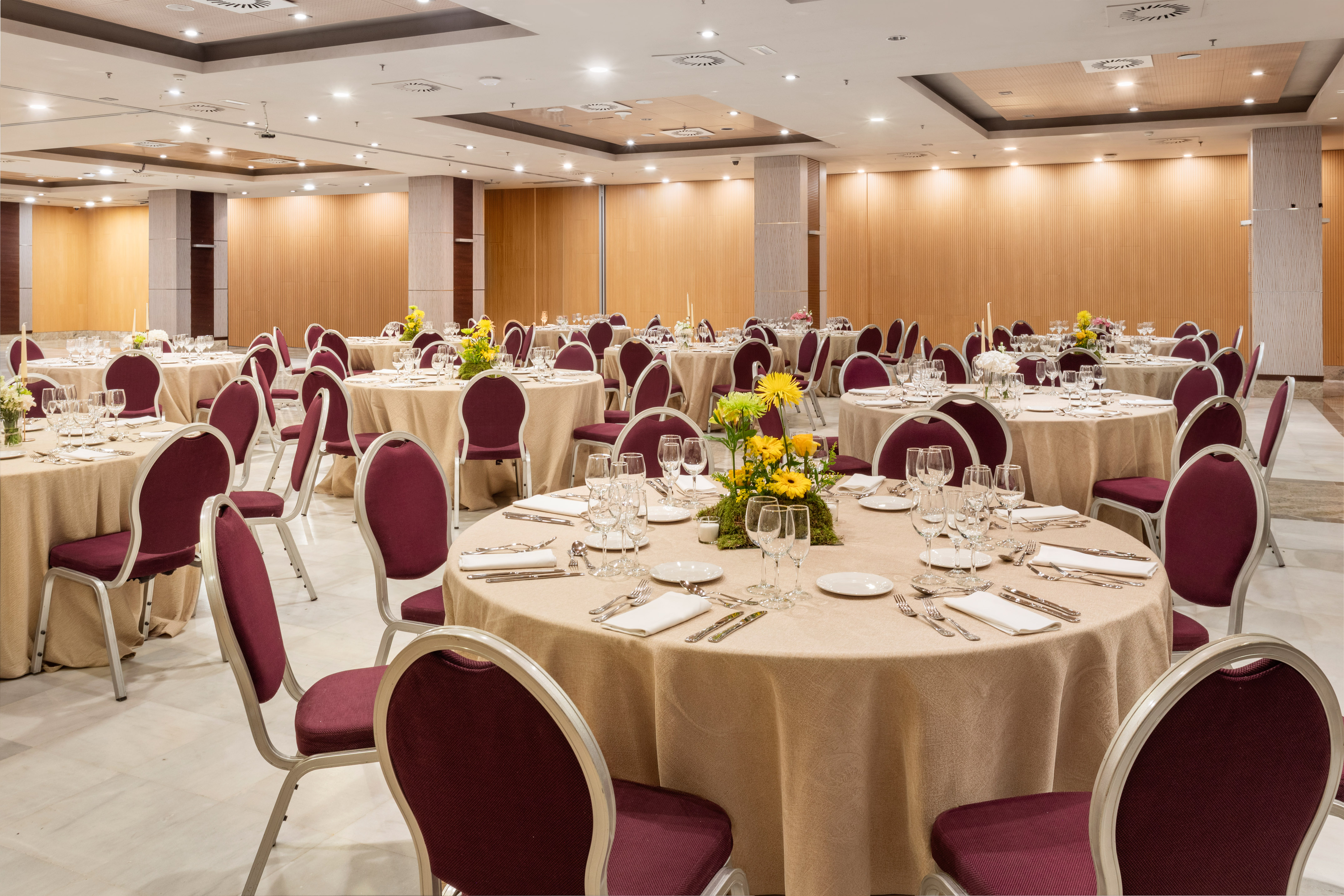 Banquet hall with round tables, maroon chairs, and yellow floral centerpieces.