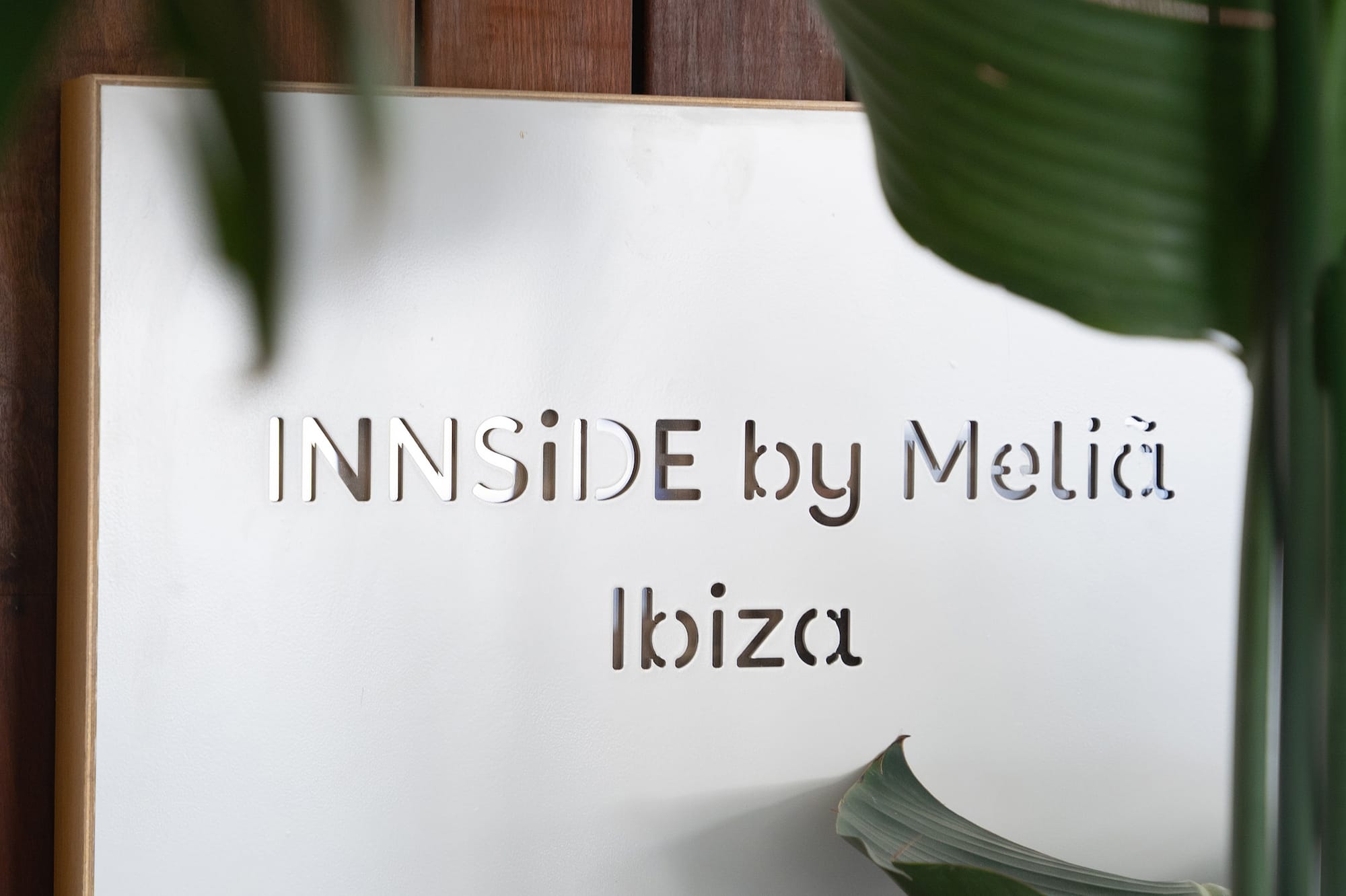 White INNSIDE by Meliã Ibiza hotel sign on wooden wall with tropical plants.