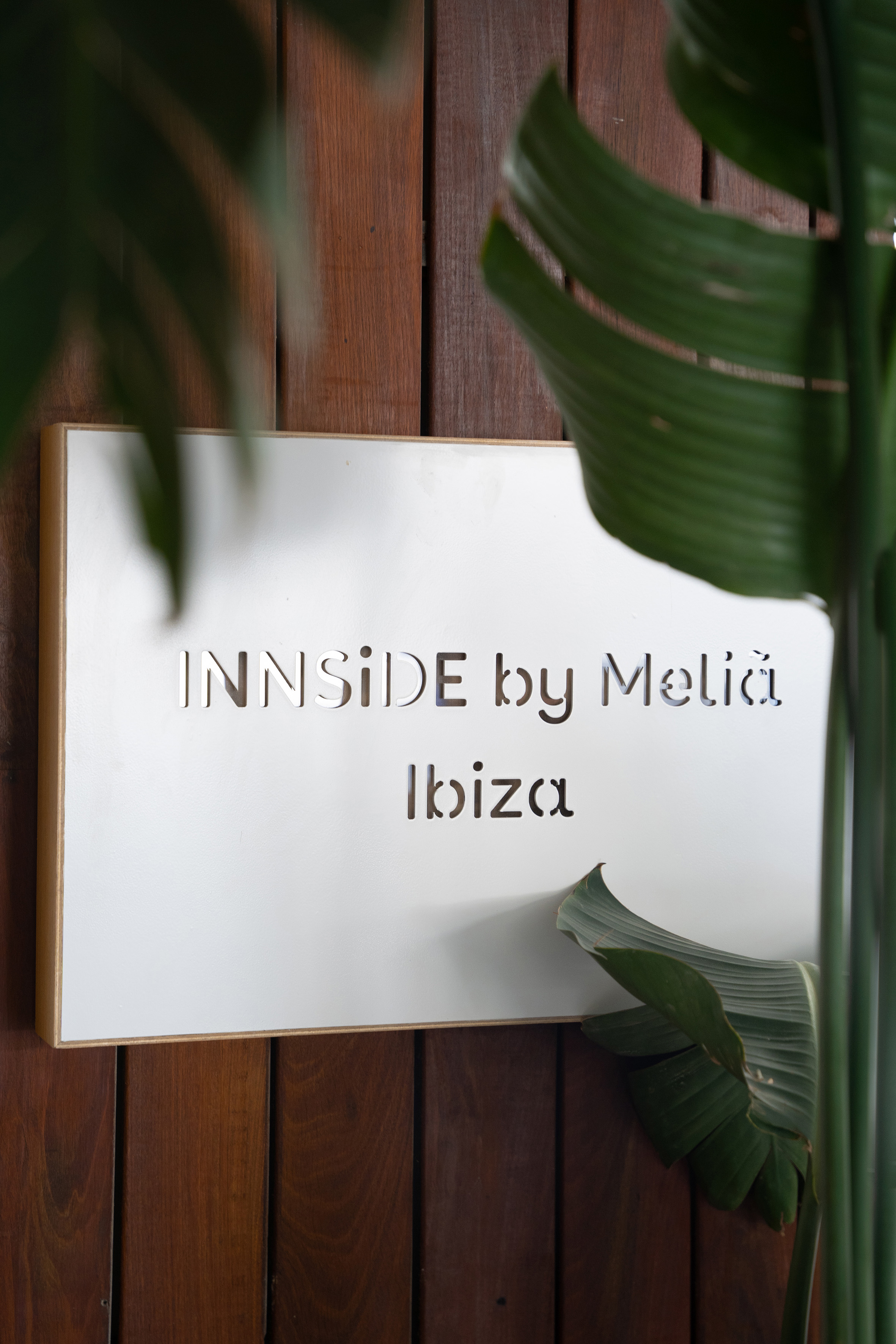 White INNSIDE by Meliã Ibiza hotel sign on wooden wall with tropical plants.