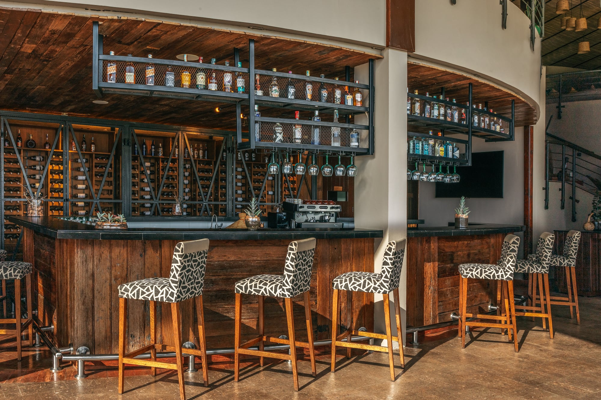 Modern rustic bar with liquor bottles, wine cellar, and patterned bar stools.