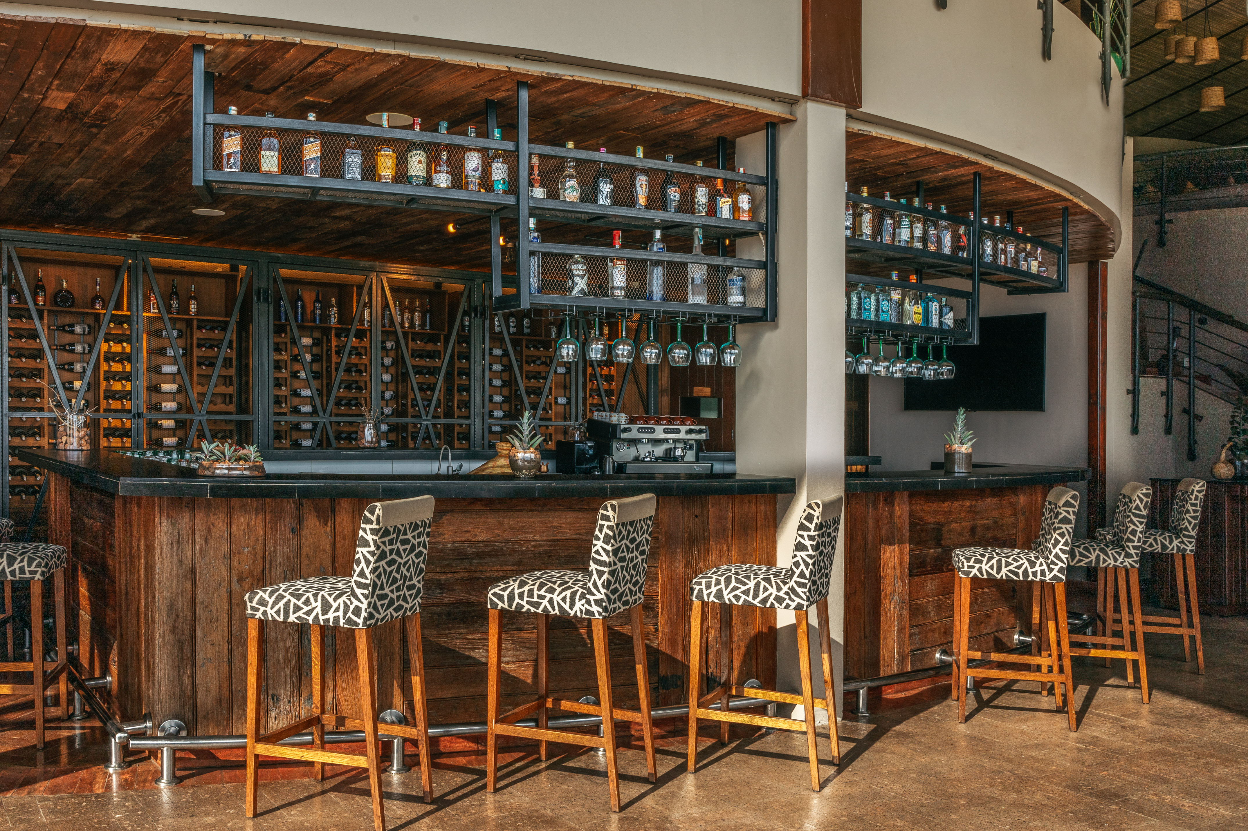 Modern rustic bar with liquor bottles, wine cellar, and patterned bar stools.