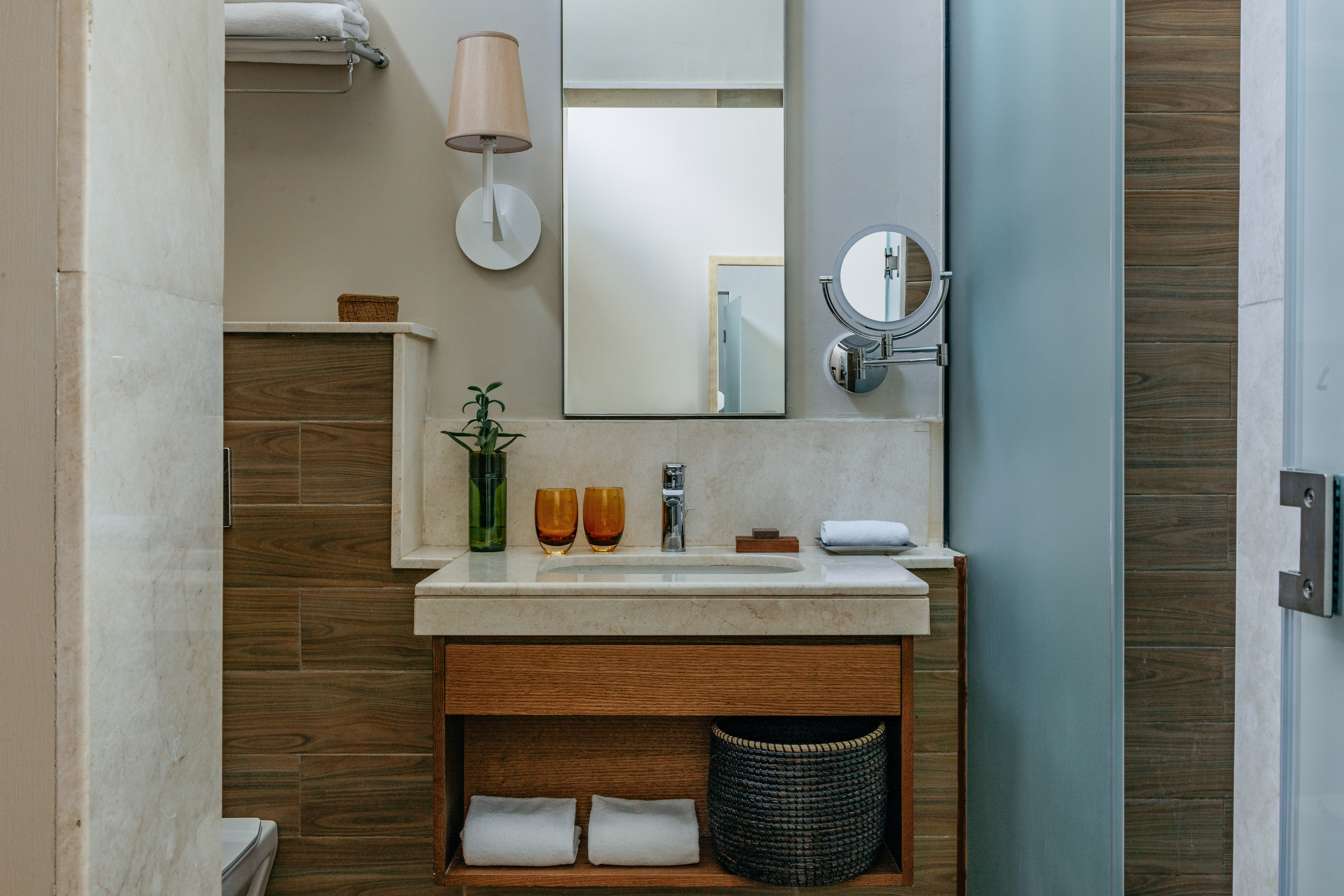 Modern bathroom vanity with marble counter, wood cabinet, sink, mirror, and plant.