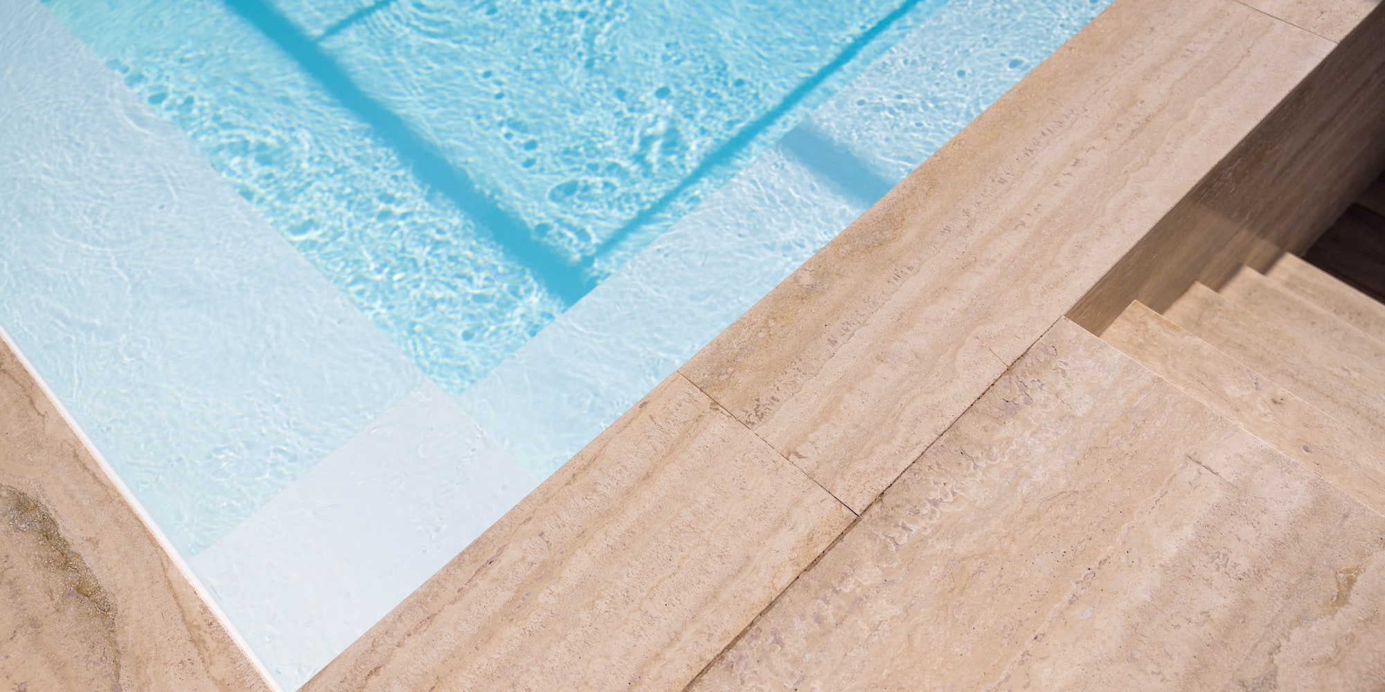Blue pool with white steps, travertine coping, and stone stairs.