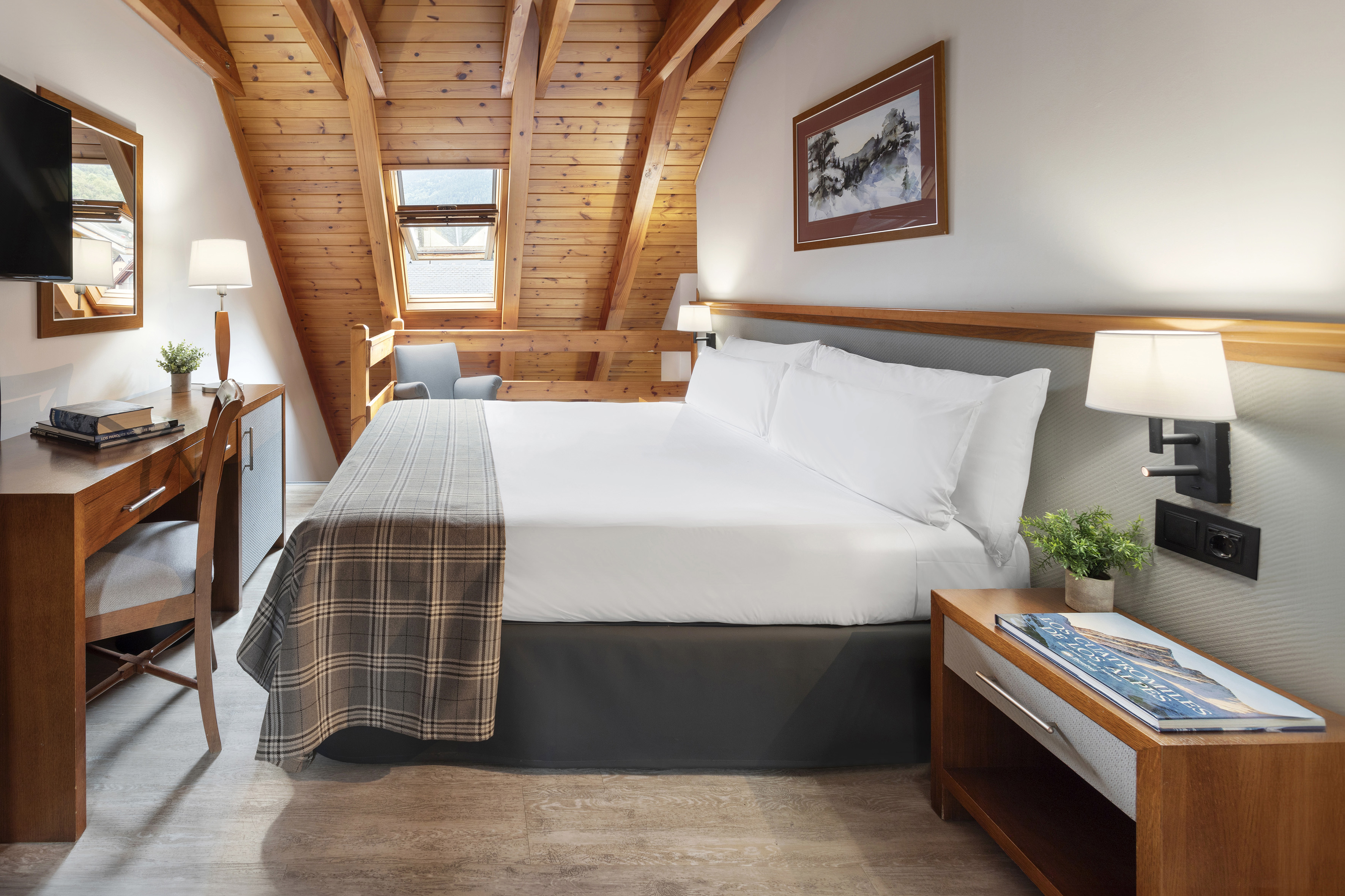 Slanted wooden ceiling hotel room with large bed, desk, and skylight.
