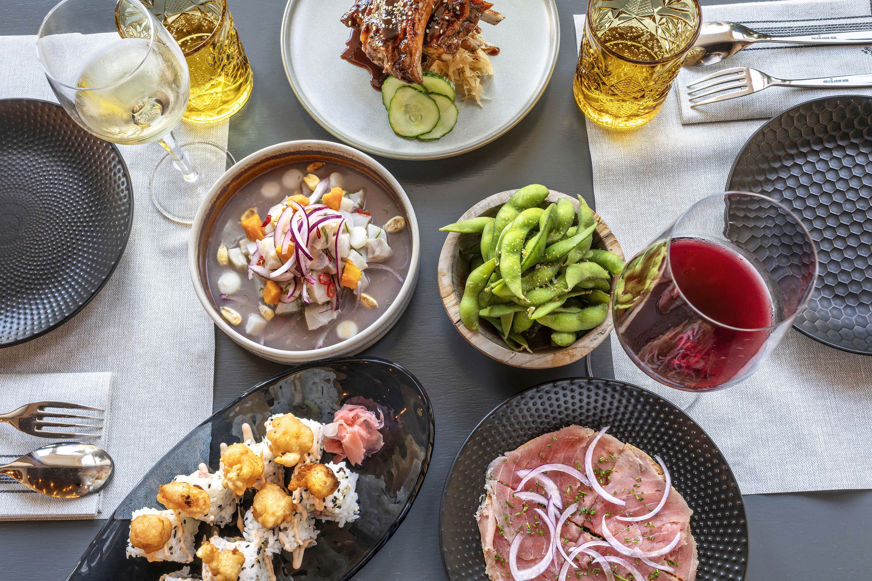 Gourmet dining spread: sushi, ceviche, edamame, meat dishes, and wine.