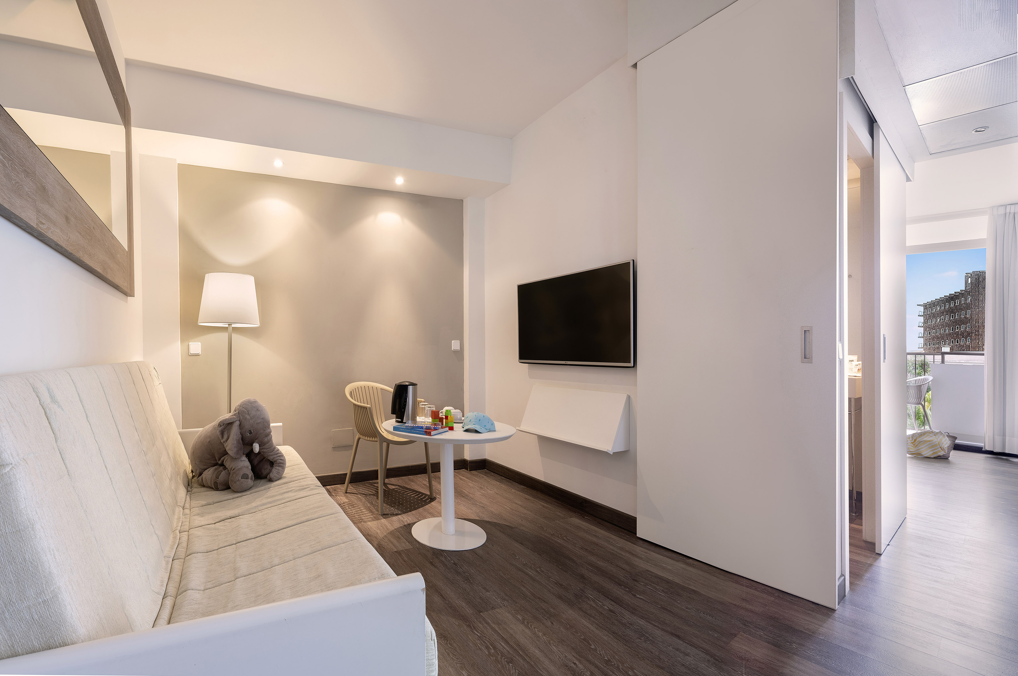 Modern family hotel suite living area with sofa, TV, play table, balcony.