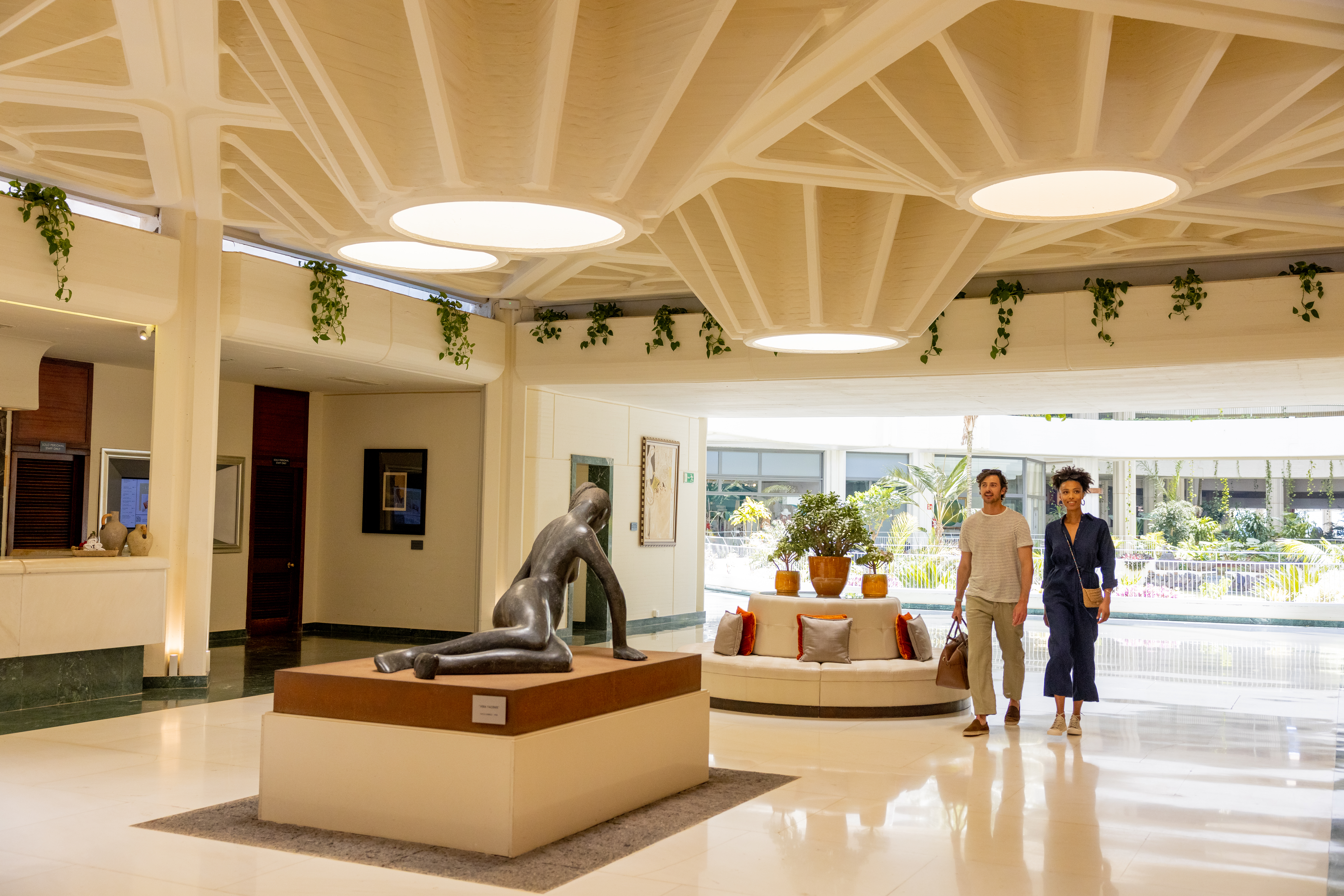 Bright hotel lobby with couple, modern sculpture, and intricate ceiling design.