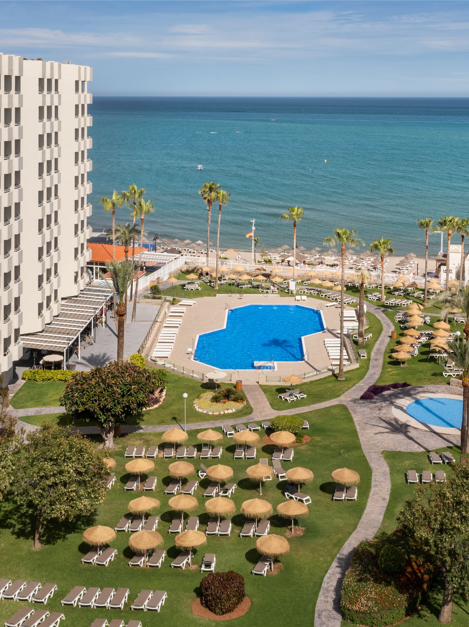 Oceanfront hotel resort with large pool, sandy beach, palm trees, and tennis court.