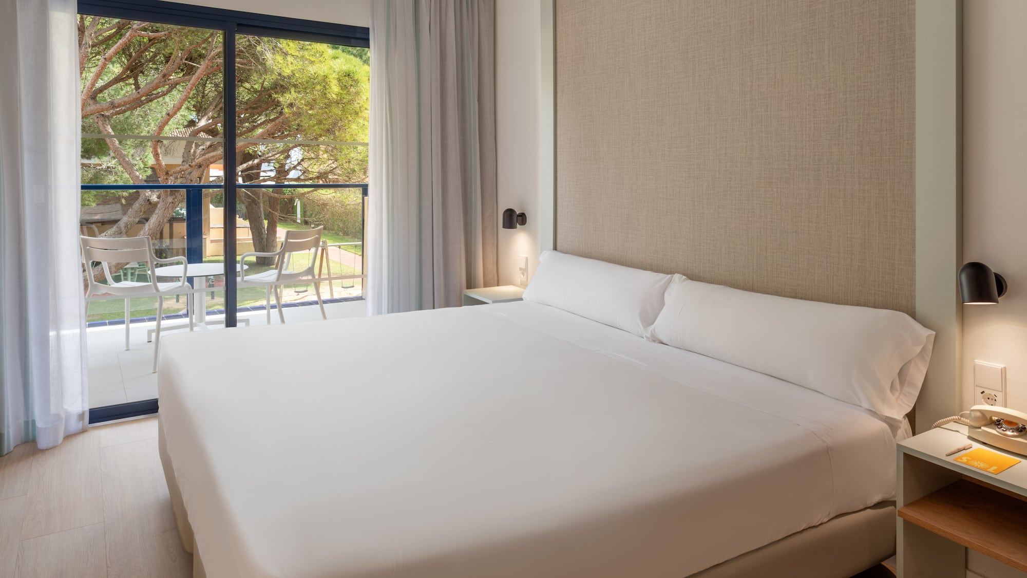 Modern hotel room with bed, balcony, and lush garden view.