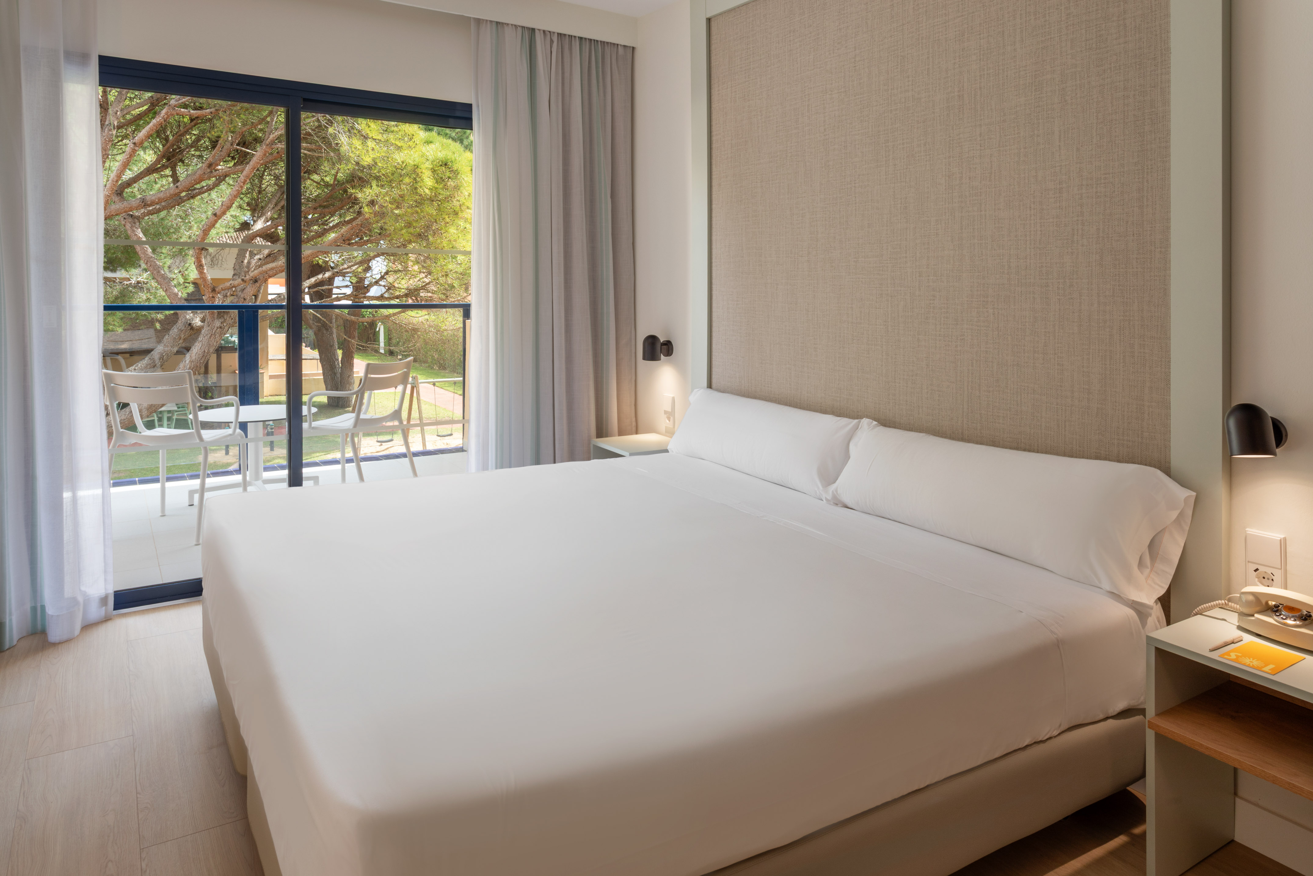 Modern hotel room with bed, balcony, and lush garden view.