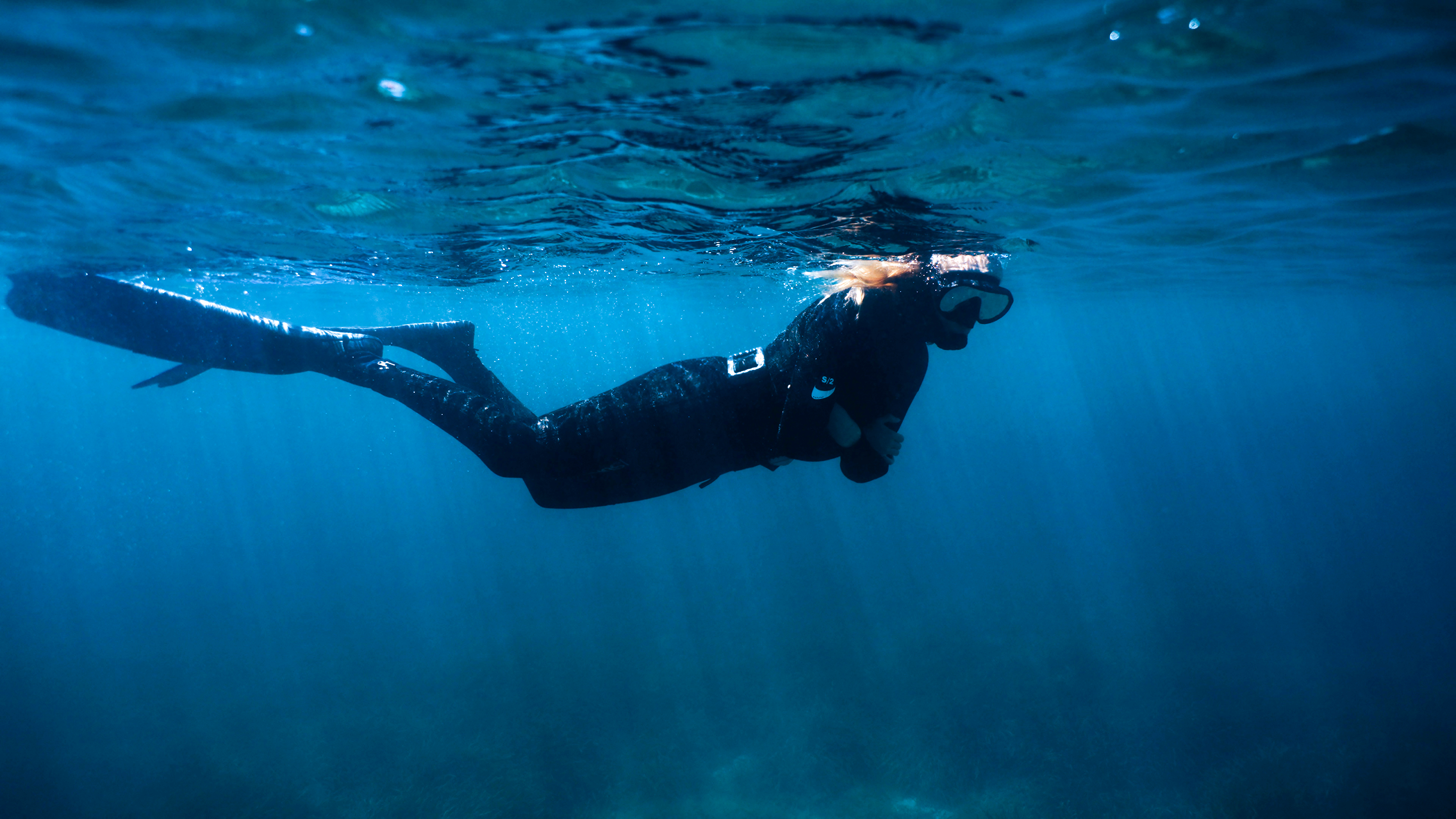 Freediver in black wetsuit, mask, and fins swimming underwater.