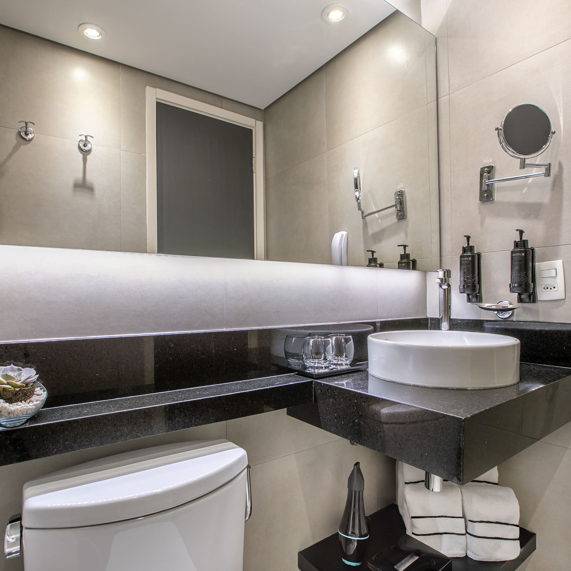 Banheiro moderno com pia branca, bancada preta e espelho iluminado. - Deluxe Room Queen - Meliá Ibirapuera, São Paulo