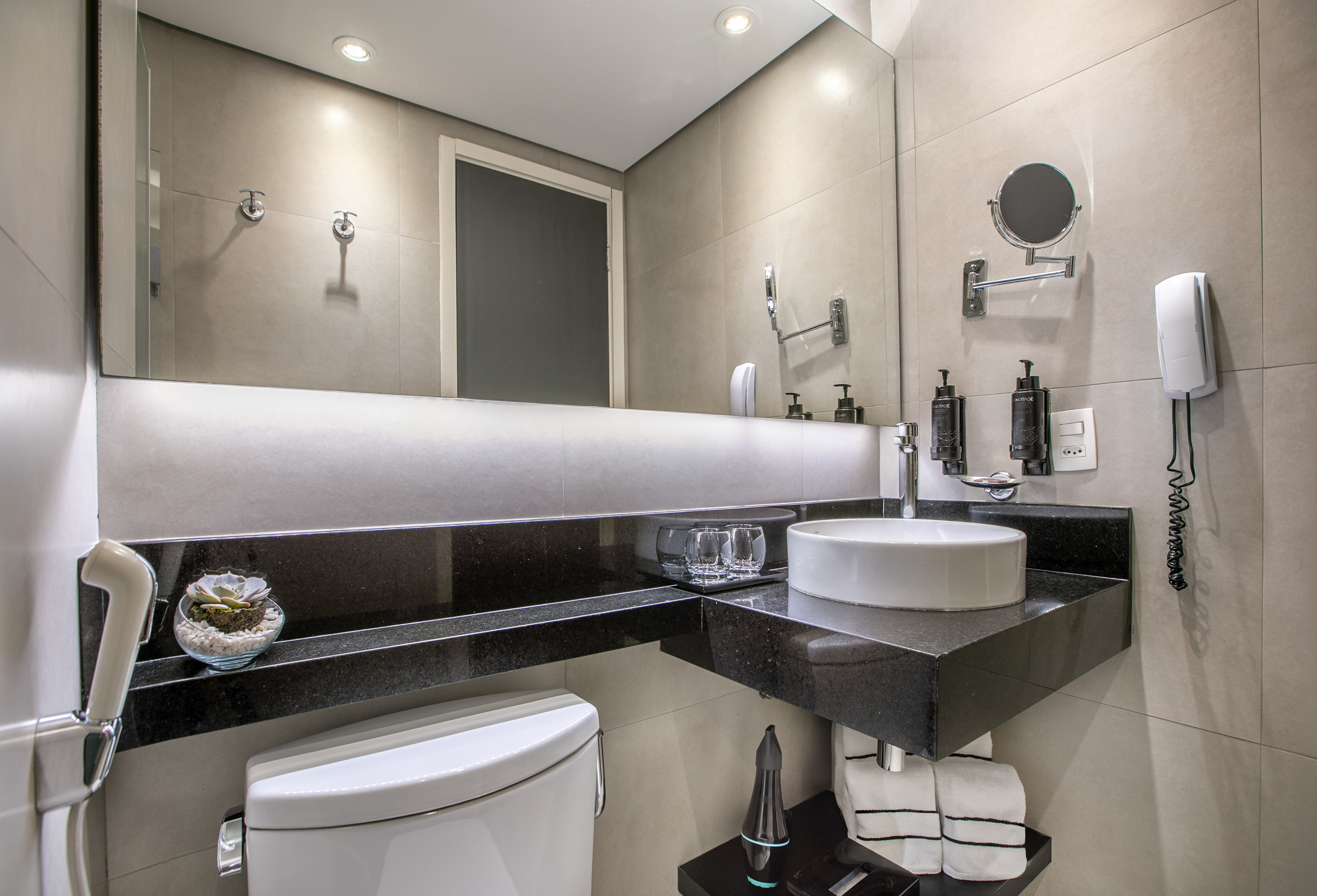 Banheiro moderno com pia branca, bancada preta e espelho iluminado. - Deluxe Room Queen - Meliá Ibirapuera, São Paulo