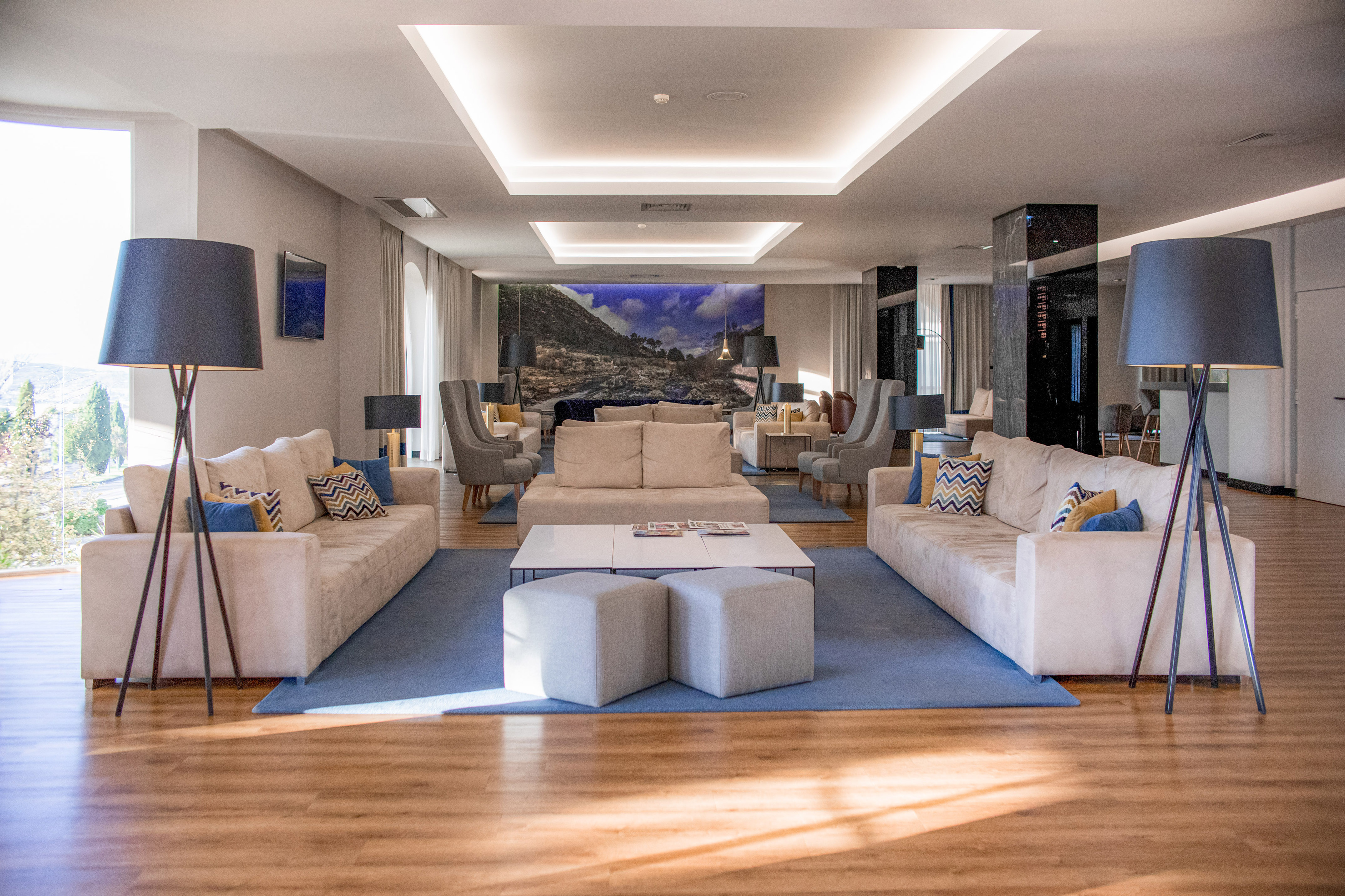 Modern hotel lounge with cream sofas, blue rugs, and a landscape wall mural.