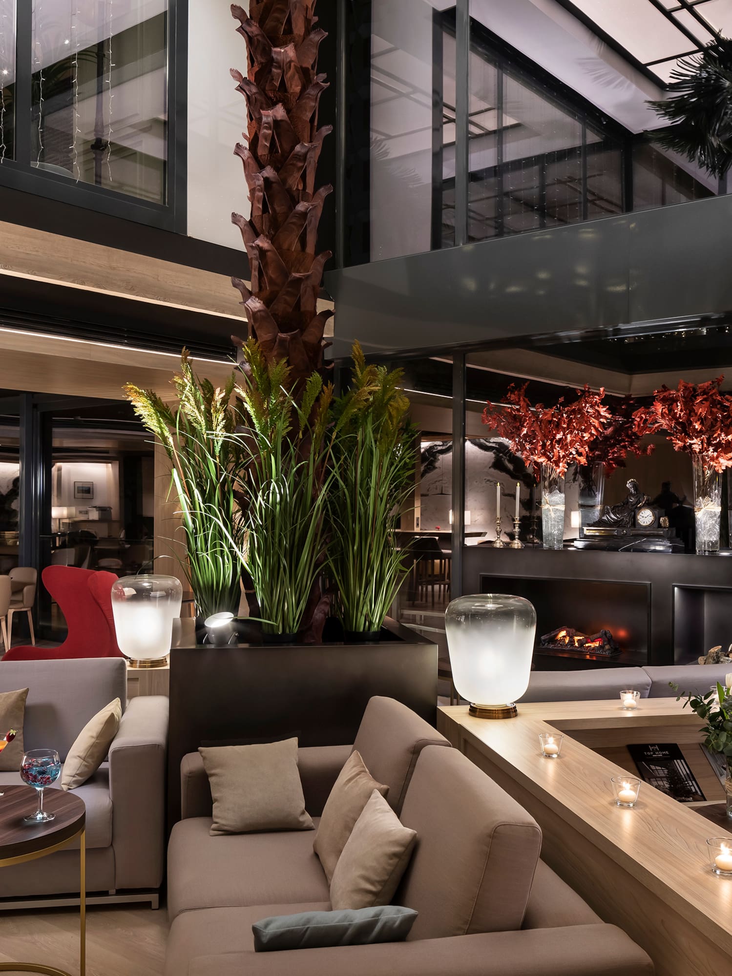 Luxury hotel lounge with modern sofas, fireplace, cocktails, and indoor plants.